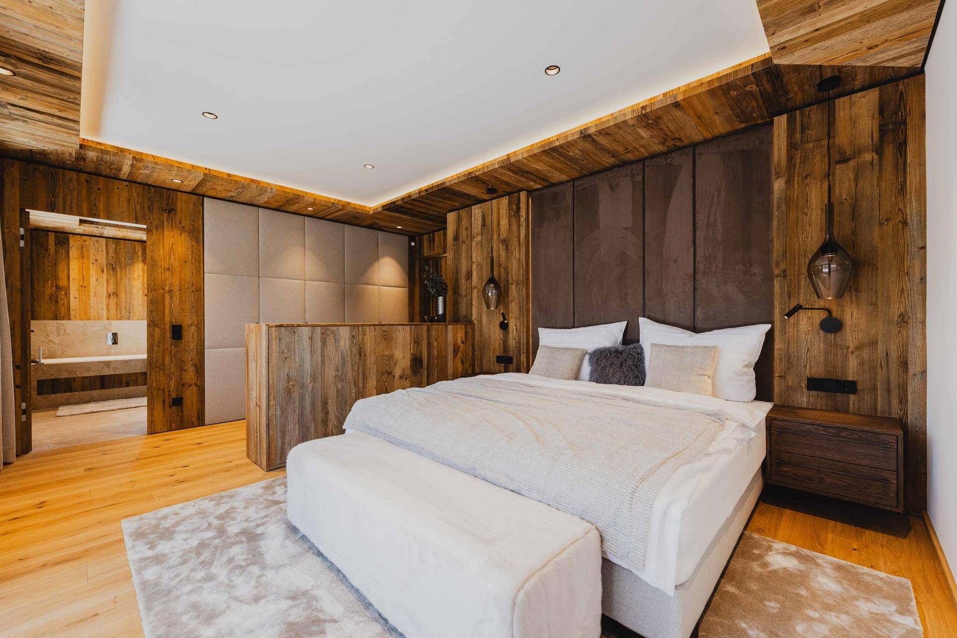 Luxuriöses Schlafzimmer mit Holzwänden, großem Bett und offenem Zugang zu einem modernen Badezimmer.