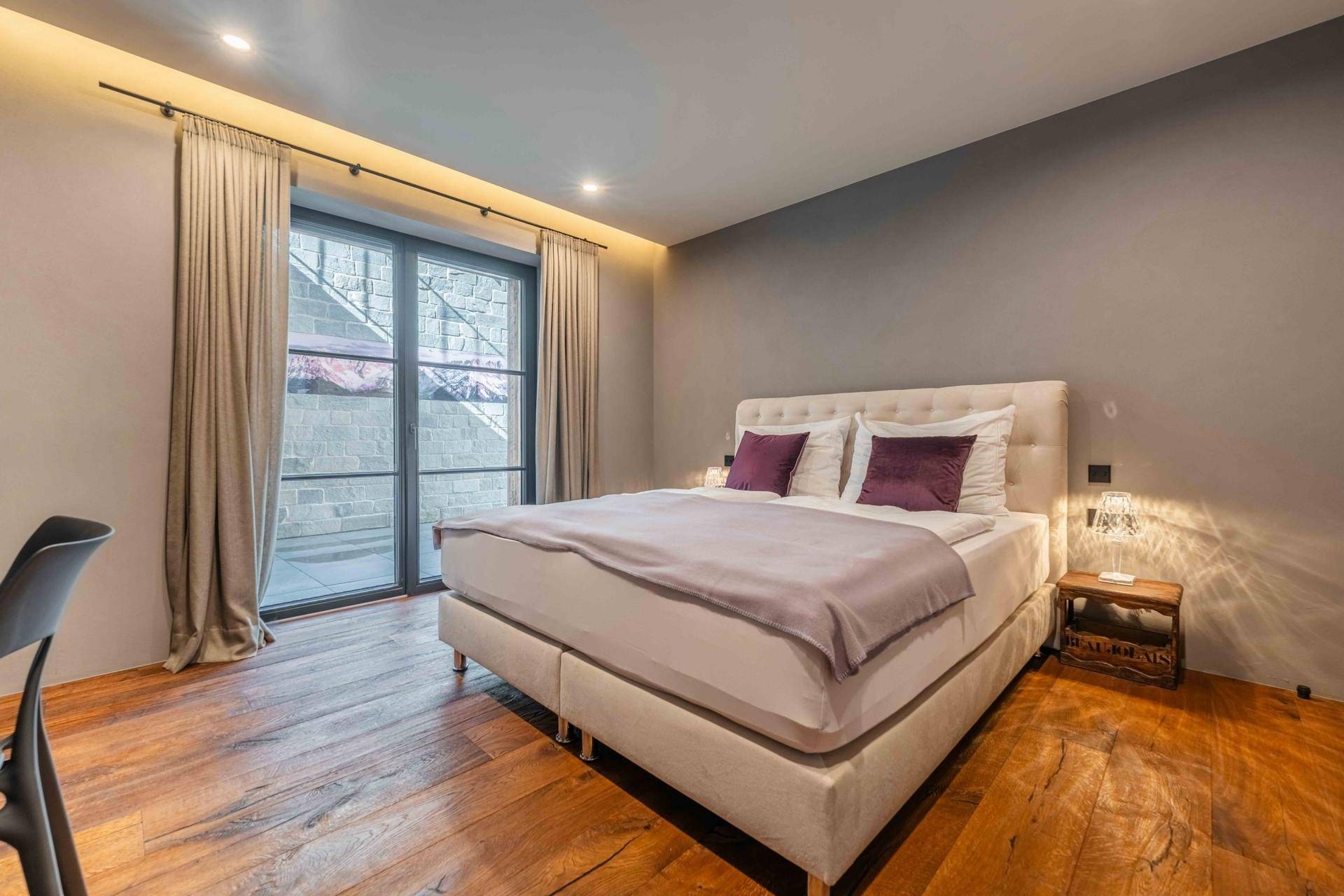 Helles Schlafzimmer mit Holzboden, großem Bett und Zugang zu einem Außenbereich.