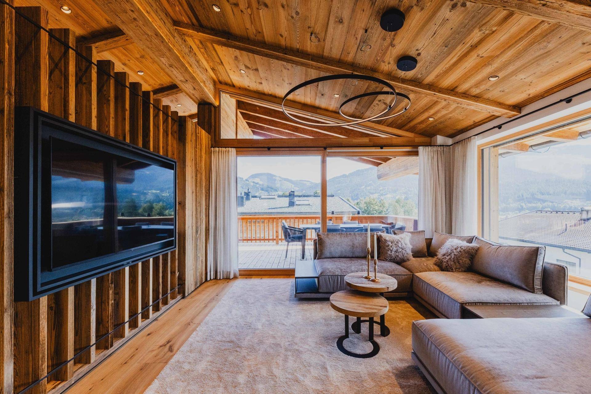 Gemütliches Wohnzimmer mit Holzwänden, großem Sofa und Zugang zu einem Balkon mit Bergblick.