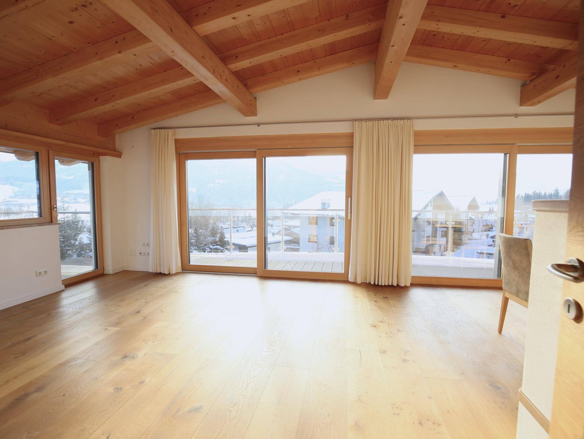 Heller Wohnbereich mit Holzbalkendecke, Parkettboden und großen Schiebetüren zu einem Balkon mit Bergblick.