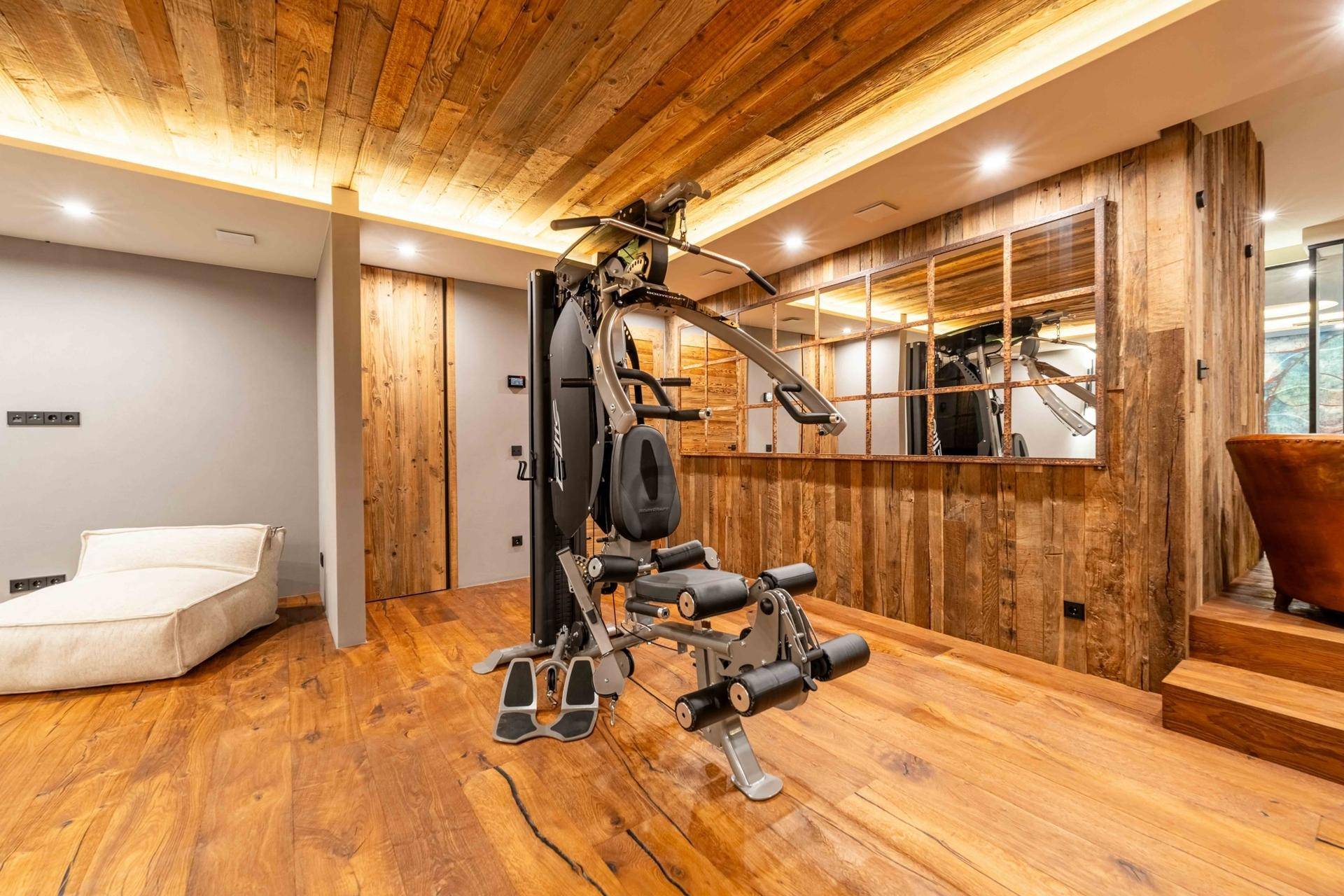 Fitnessbereich mit Trainingsgerät, Holzboden und Spiegelwand für das tägliche Workout.