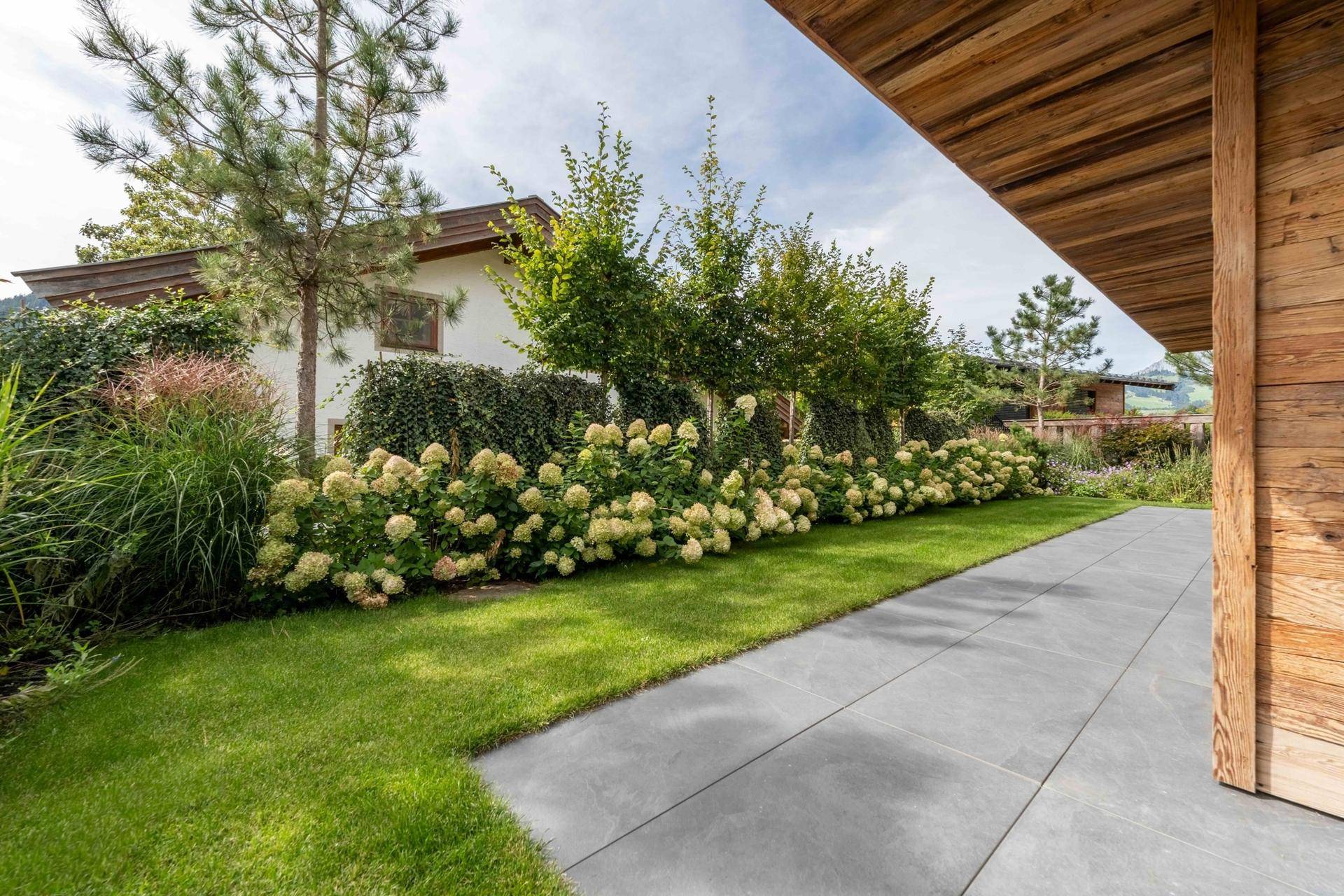 Weitläufiger Gartenbereich mit gepflegtem Rasen, blühenden Hortensien und moderner Holzfassade.