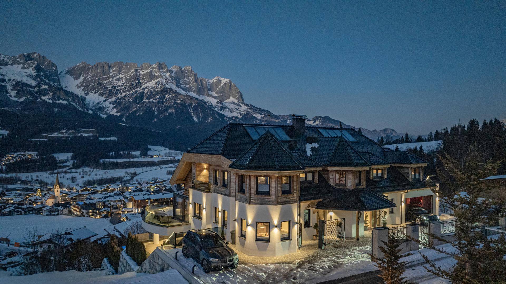 Beleuchtetes Luxusanwesen in alpiner Landschaft bei Nacht mit verschneiter Umgebung.