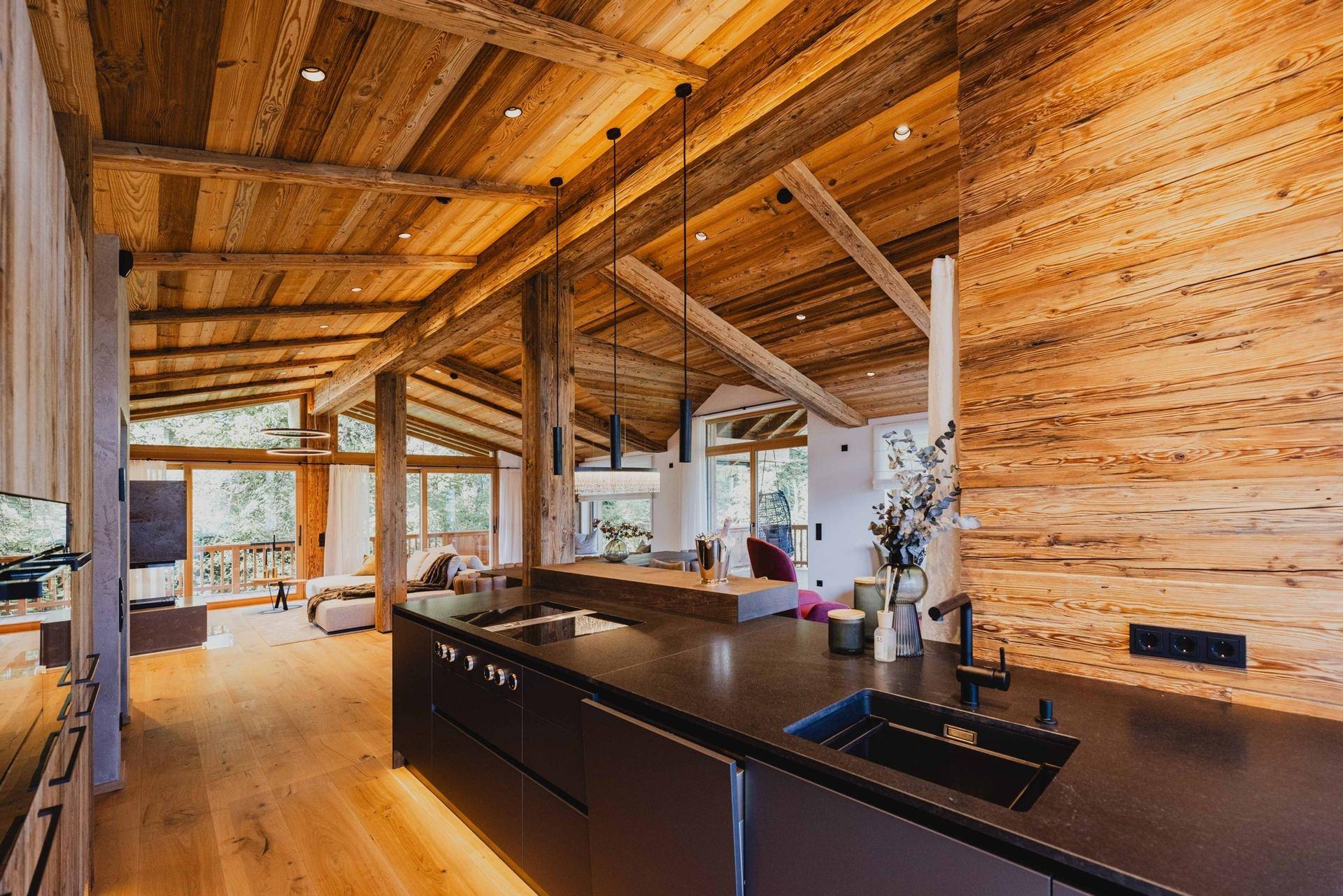 Elegante offene Küche mit dunkler Arbeitsplatte, Induktionskochfeld und Holzbalkendecke.