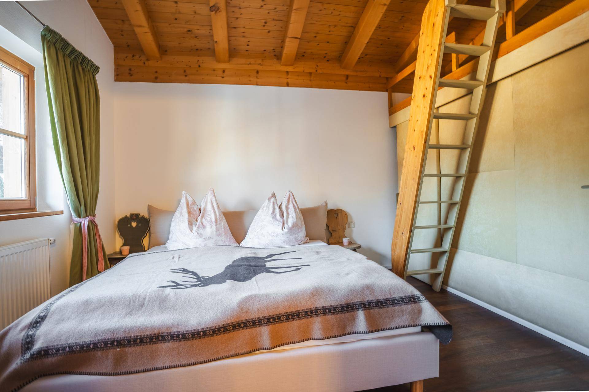 Schlafzimmer im alpinen Stil mit Holzbalkendecke, Leiter zum Hochbett und Hirschmotiv.