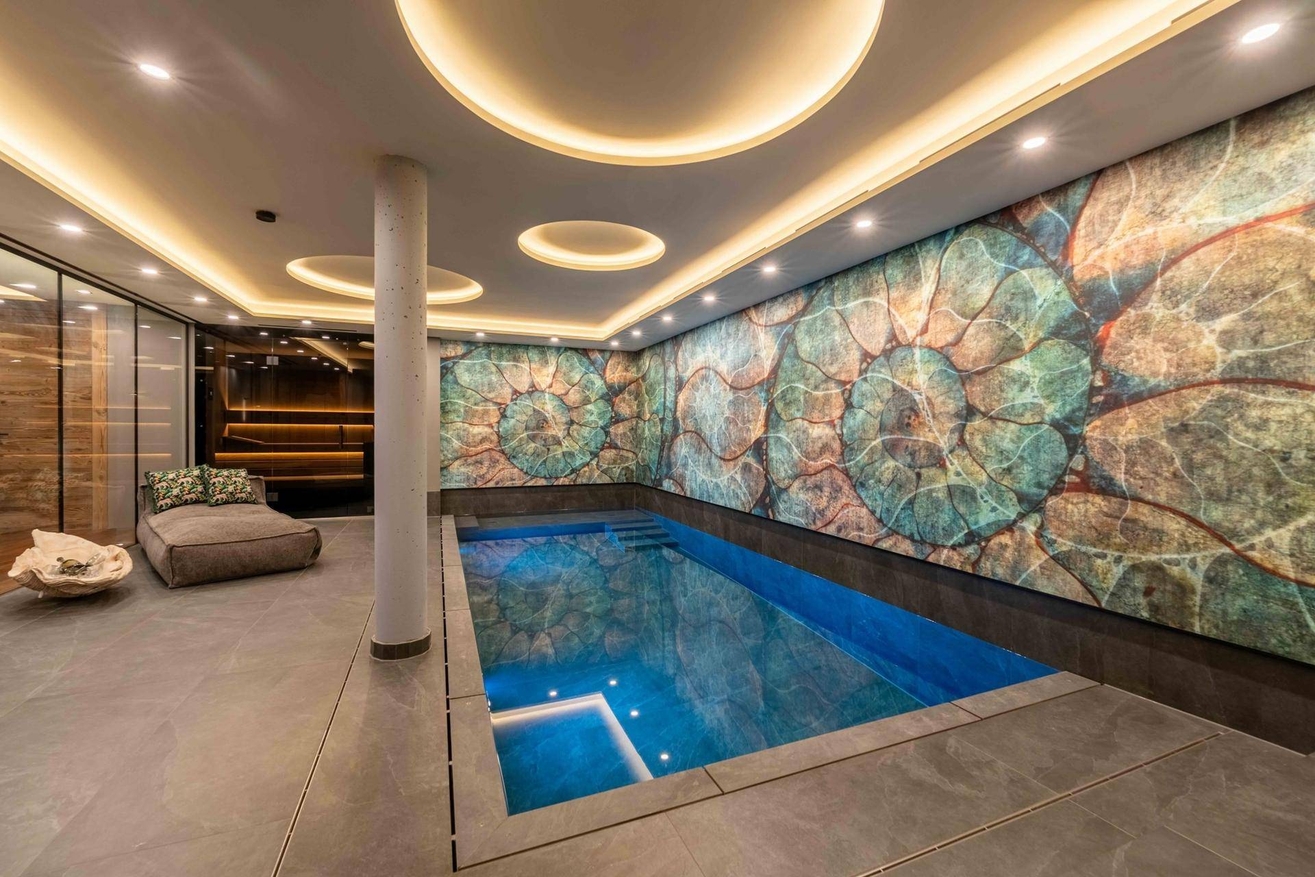 Moderner Innenpool mit Unterwasserbeleuchtung und kunstvoller Wanddekoration in einem Wellnessbereich.