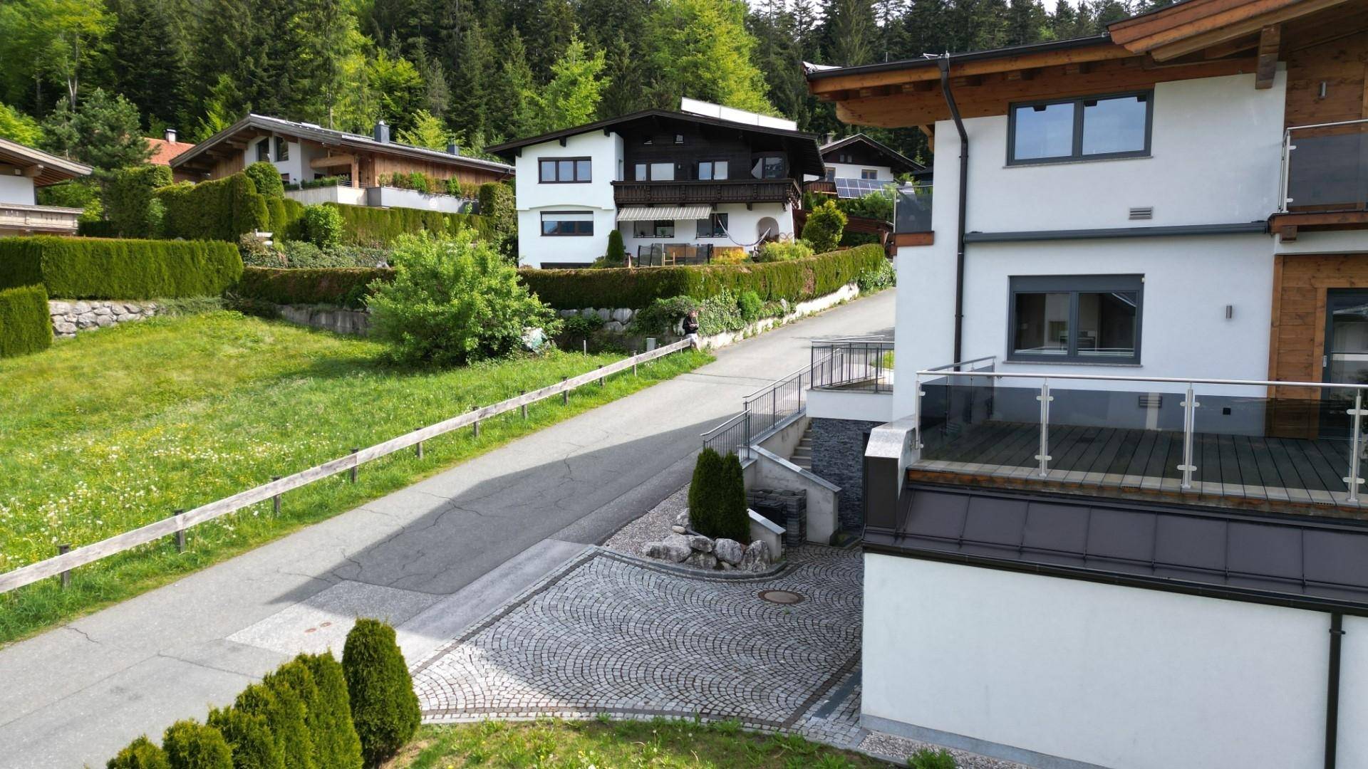 Zufahrt zum modernen Wohnhaus mit gepflastertem Bereich und umliegender Grünfläche in Hanglage.
