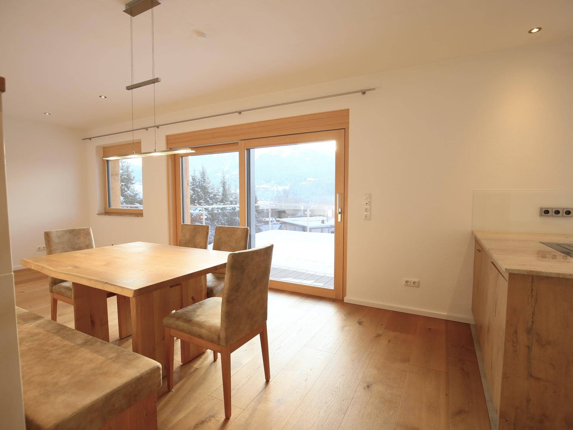 Heller Essbereich mit Holztisch und Blick durch die großen Fenster auf die winterliche Umgebung.