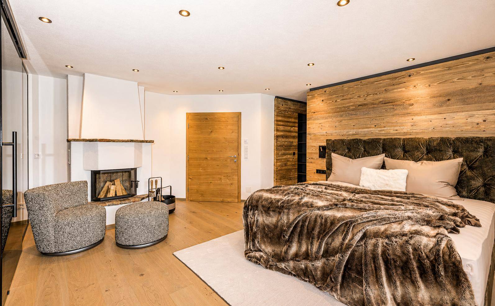 Gemütliches Schlafzimmer mit großem Bett, Kamin und Holzwandverkleidung.