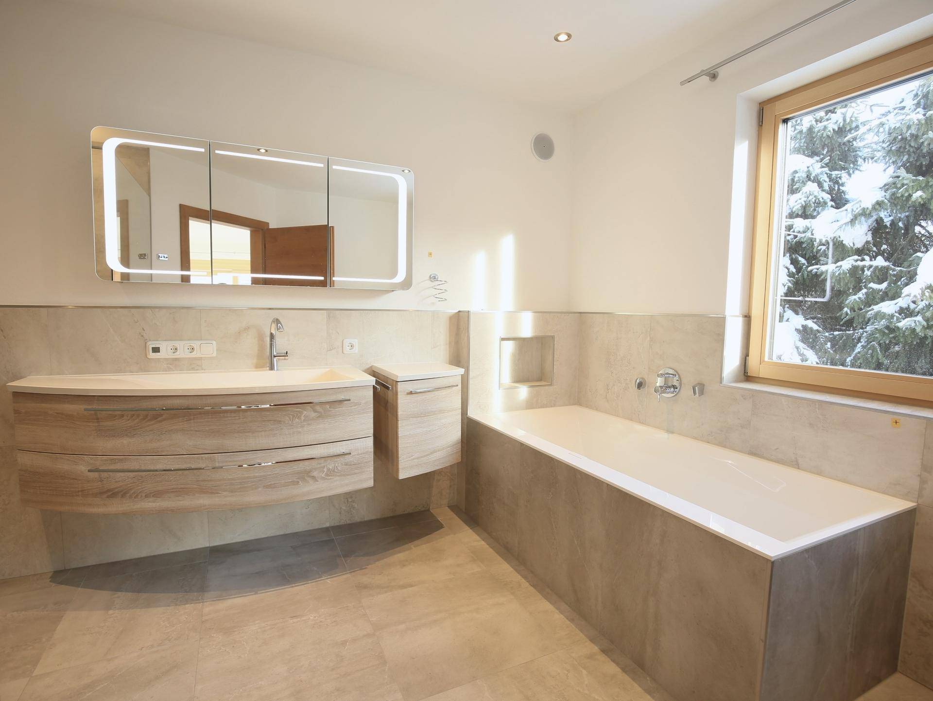 Modernes Badezimmer mit Badewanne, Einzelwaschbecken und Fenster mit Winterblick.