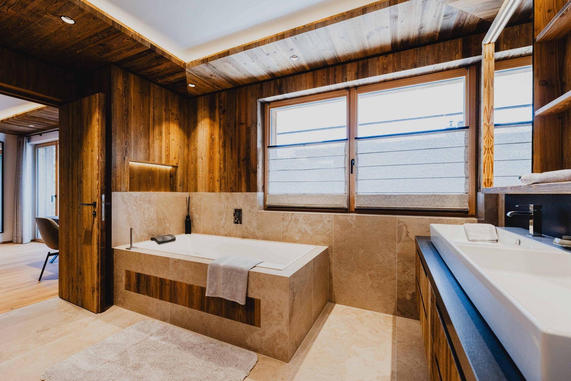 Helles Badezimmer mit Badewanne, Doppelwaschbecken und Fenster für Tageslicht.