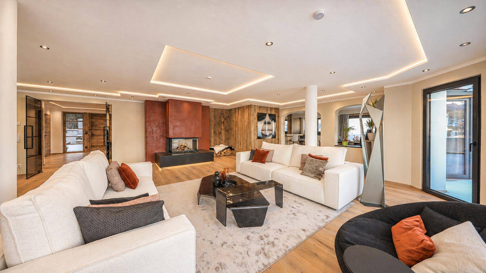 Großzügiges Wohnzimmer mit Kamin, mehreren Sofas und indirekter Deckenbeleuchtung.
