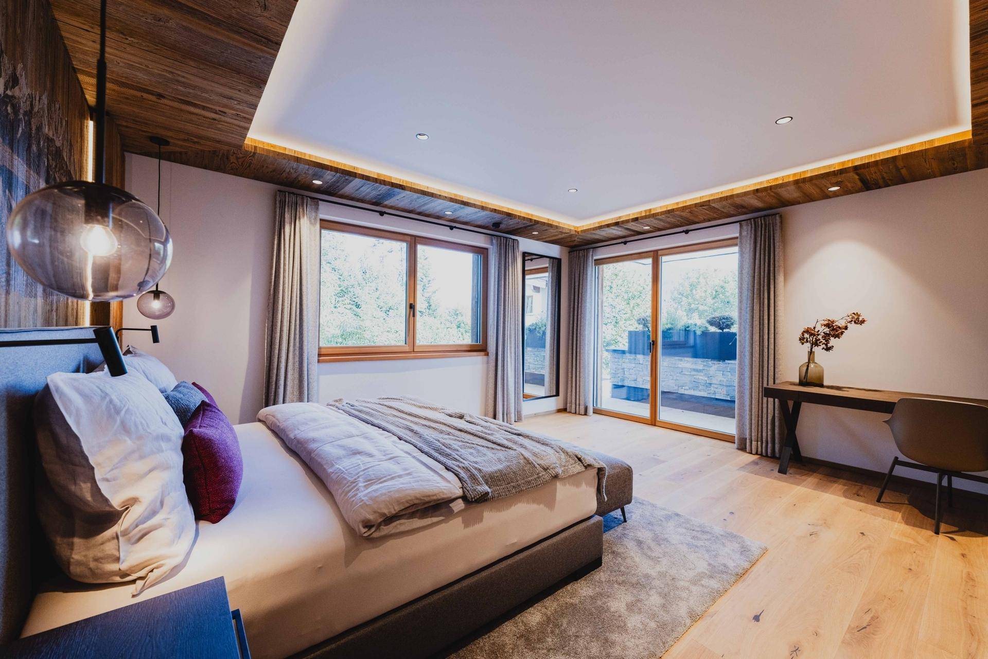 Helles Schlafzimmer mit Holzboden, großen Fenstern und Zugang zu einem Außenbereich.