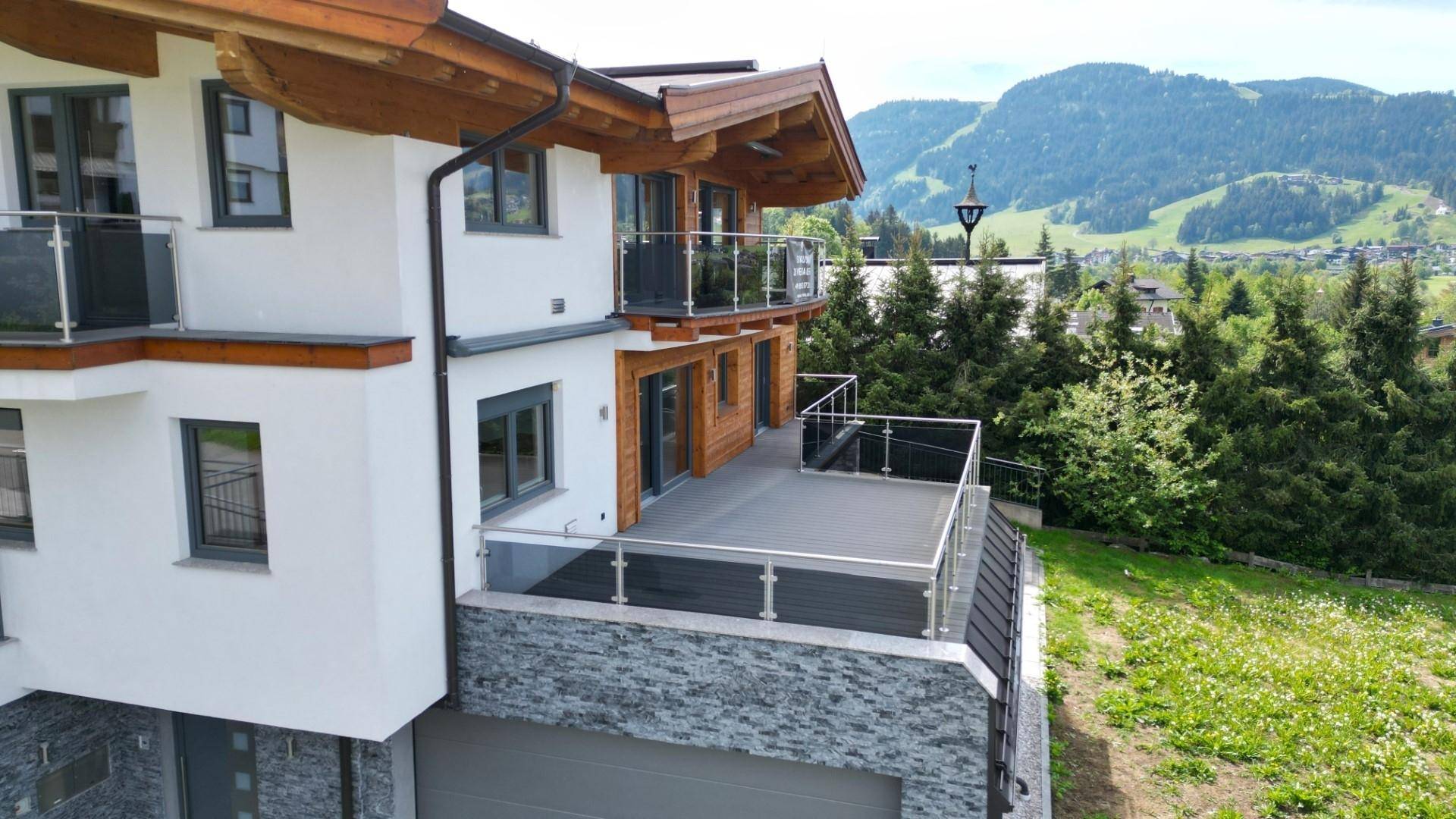 Große Terrasse mit Glasgeländer und Blick auf die umliegende Berglandschaft und Wälder.