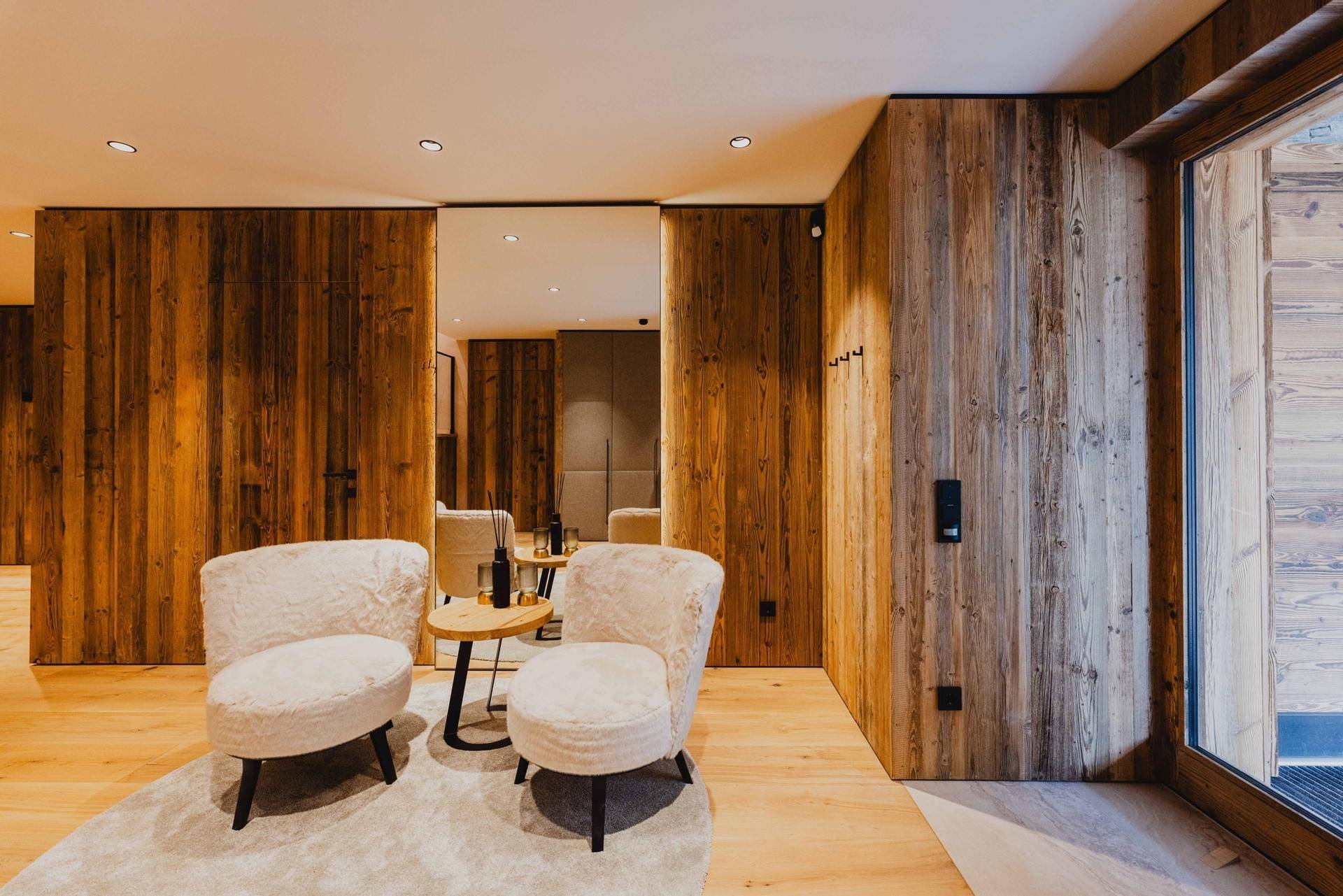 Gemütlicher Lounge-Bereich im Flur mit Holzwänden, weichen Sesseln und Zugang nach draußen.