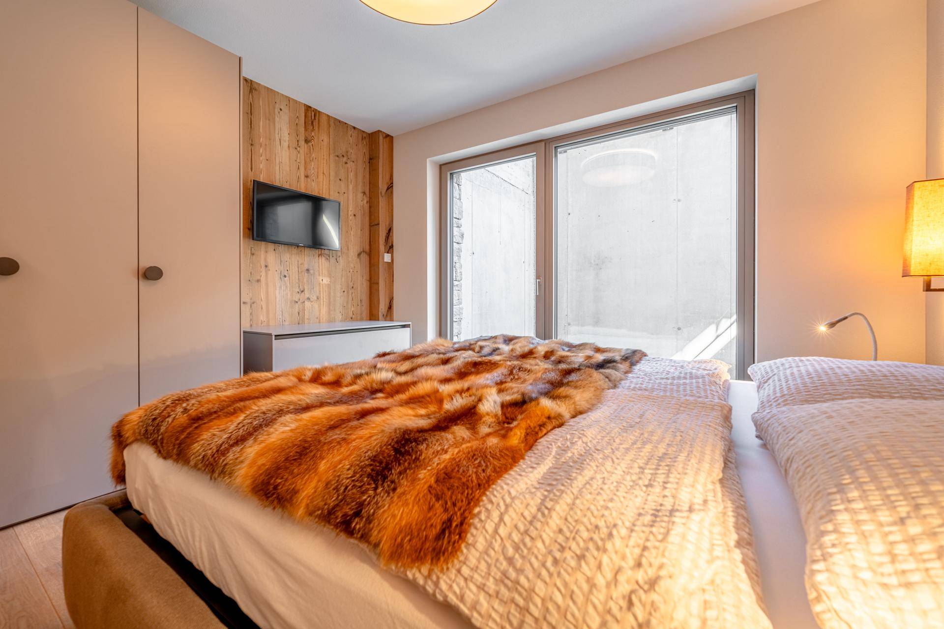 Schlafzimmer mit Holzwandverkleidung, großem Bett und Zugang zu einem Außenbereich.