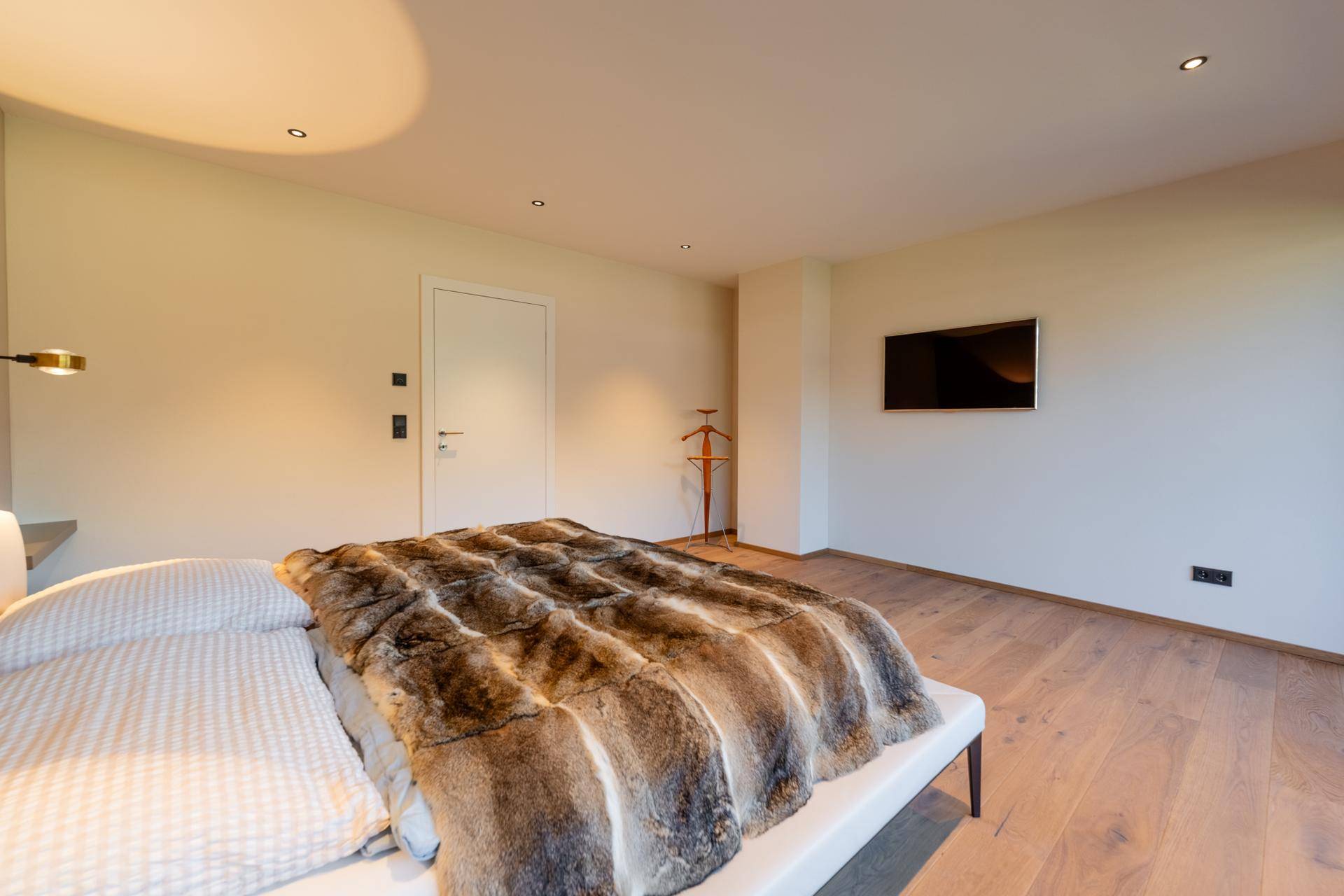 Schlafzimmer mit Holzboden, Wandfernseher und schlichter, moderner Einrichtung.