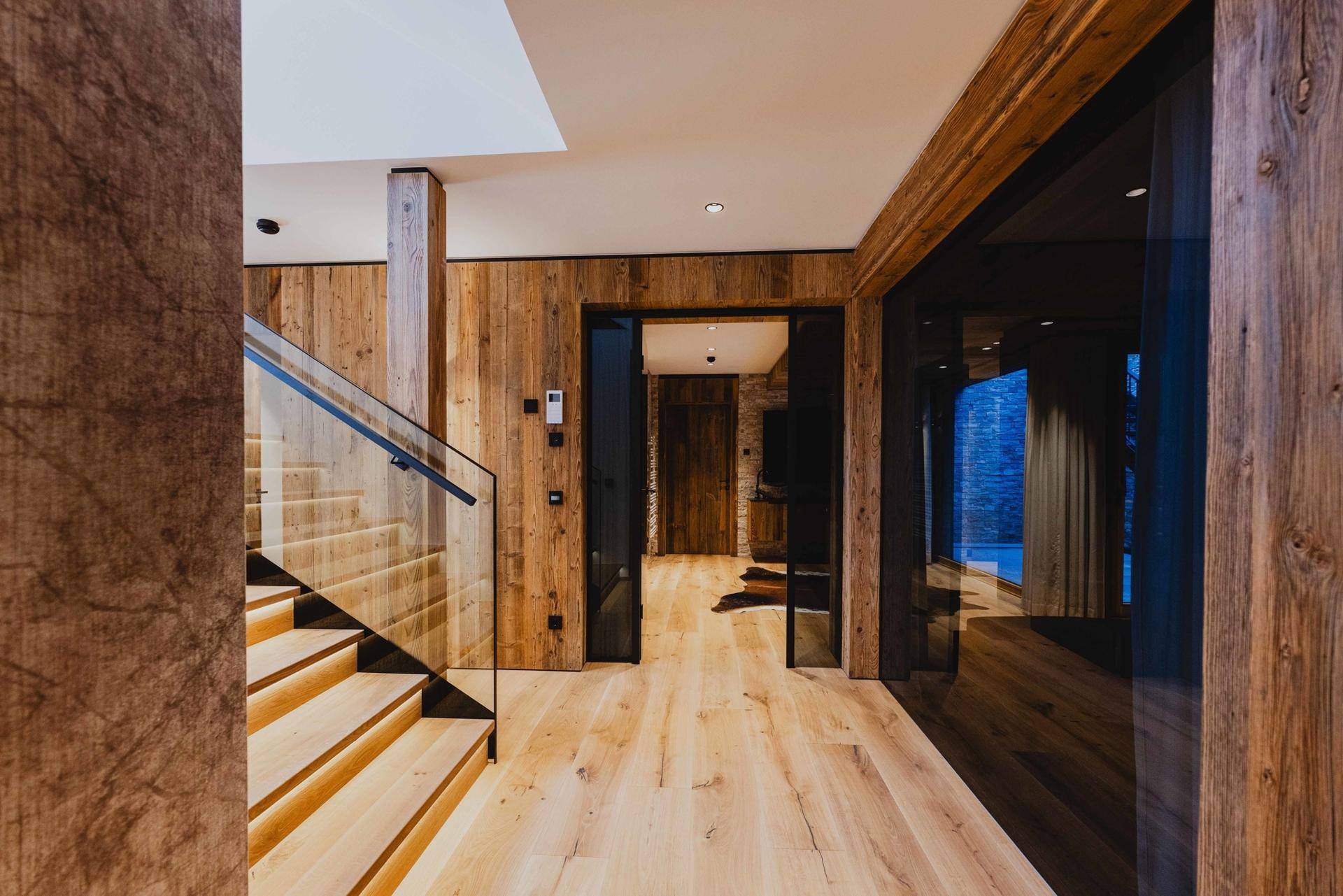 Heller Flur mit Holztreppe, Glasgeländer und Holzwänden, die Wärme ausstrahlen.