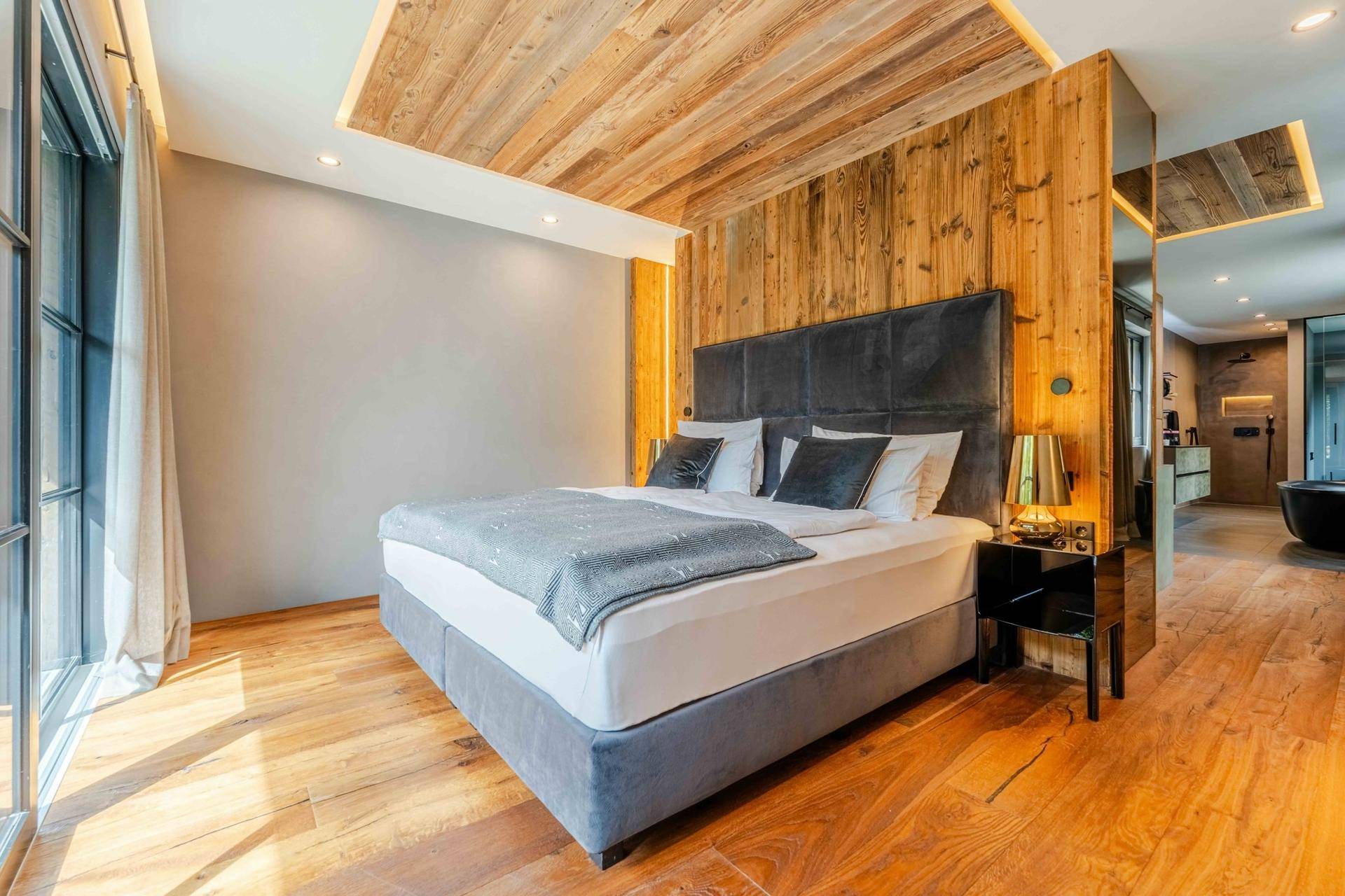 Luxuriöses Schlafzimmer mit Holzboden, großem Bett und Zugang zu einem angrenzenden Badbereich.