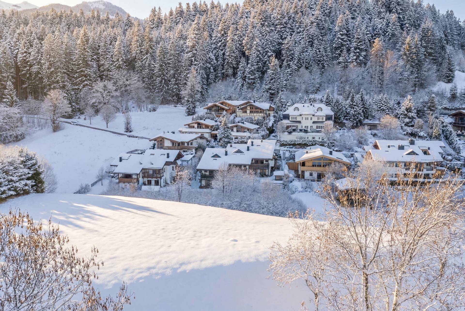 Idyllische Winterlandschaft mit schneebedeckten Häusern und Bäumen, umgeben von verschneiten Bergen.