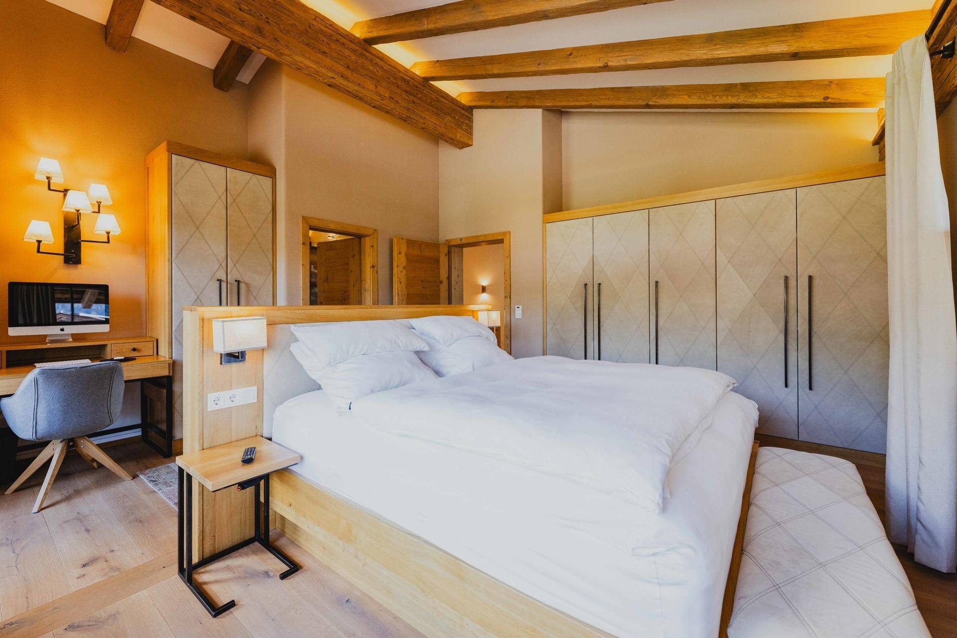 Elegantes Schlafzimmer mit Holzbalken, Einbauschränken und einem Arbeitsbereich mit Computer.