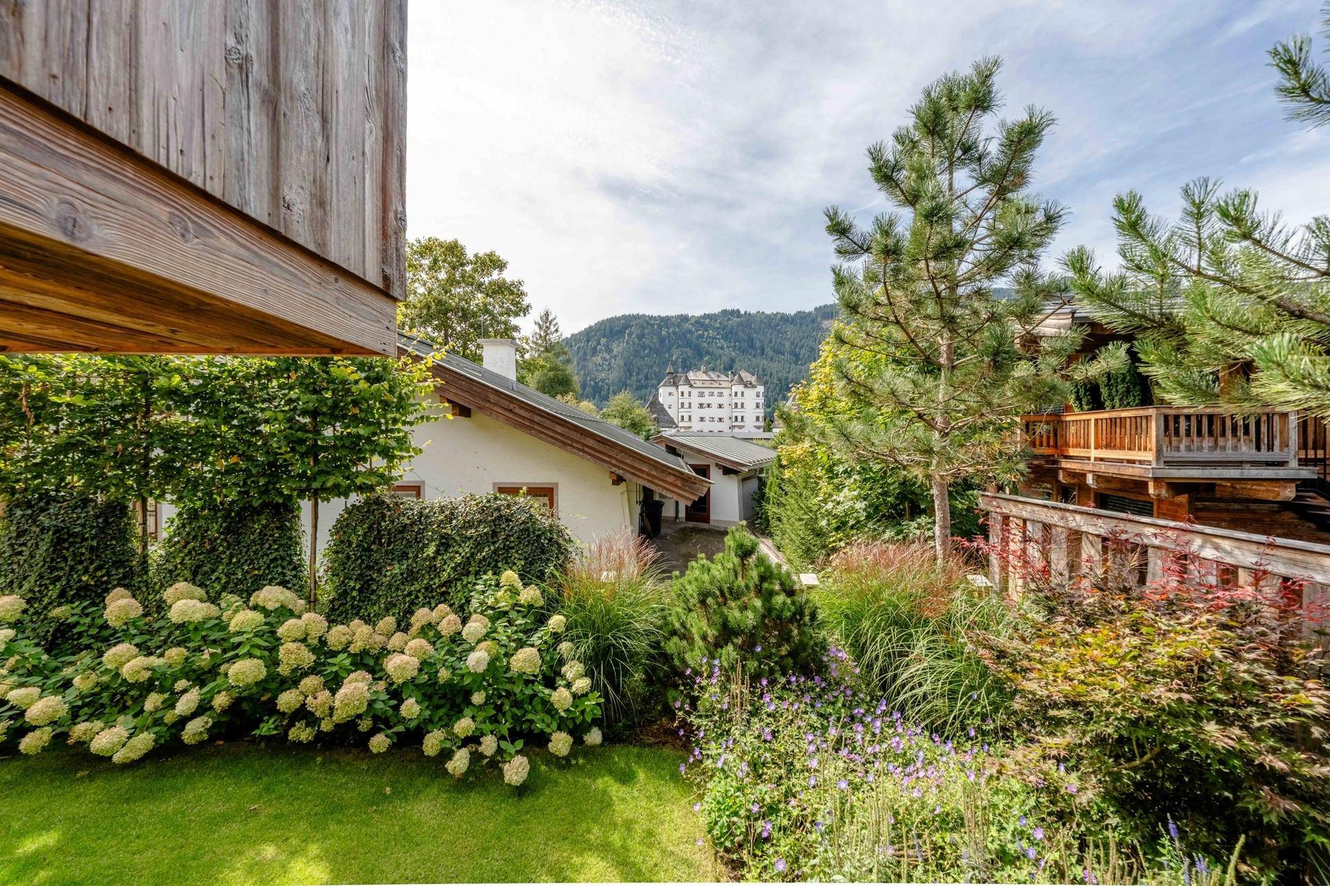 Üppiger Garten mit vielfältiger Bepflanzung, Bäumen und Blick auf die umliegende Berglandschaft.