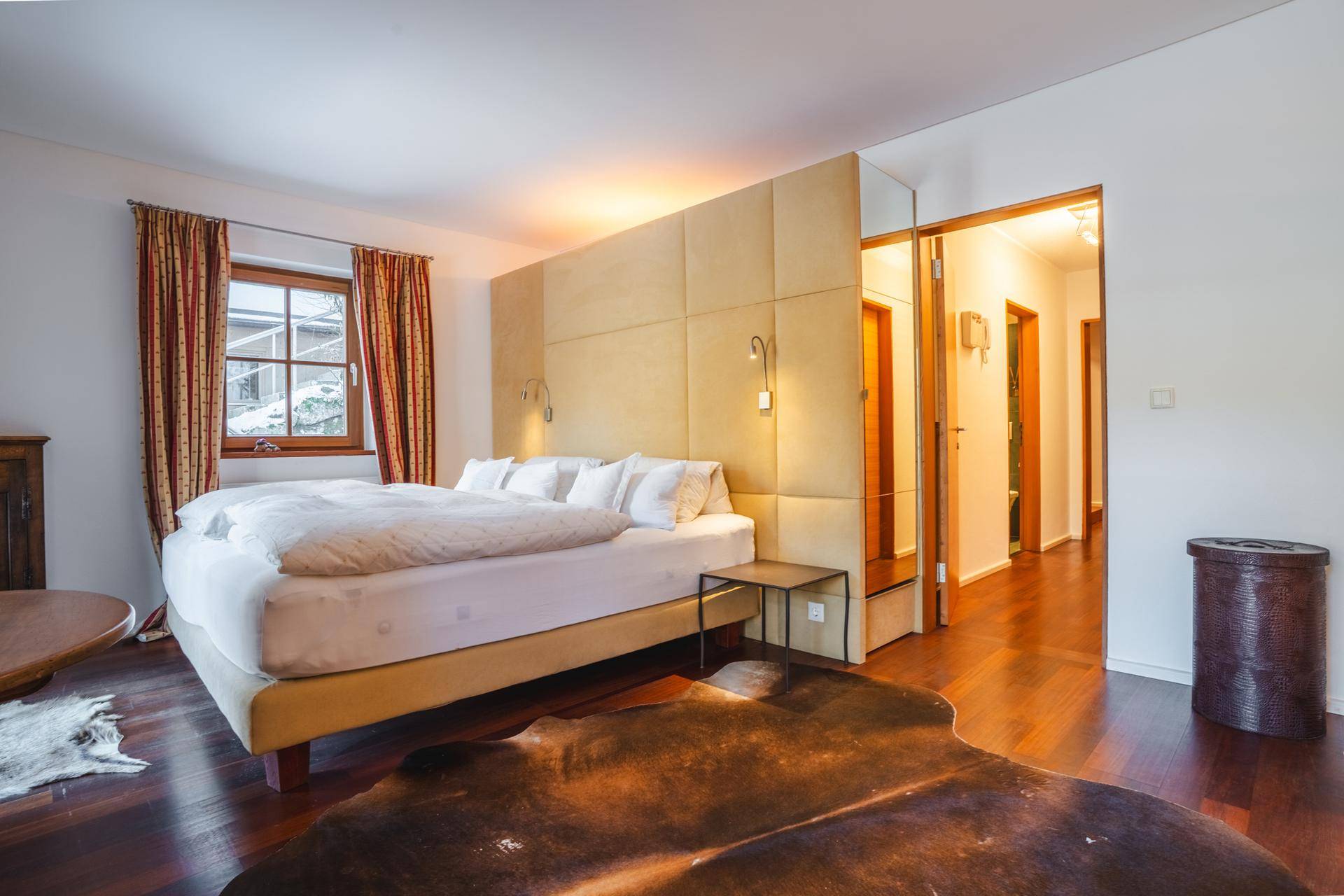Gemütliches Schlafzimmer mit großem Bett, Holzboden und Zugang zu einem Flur.