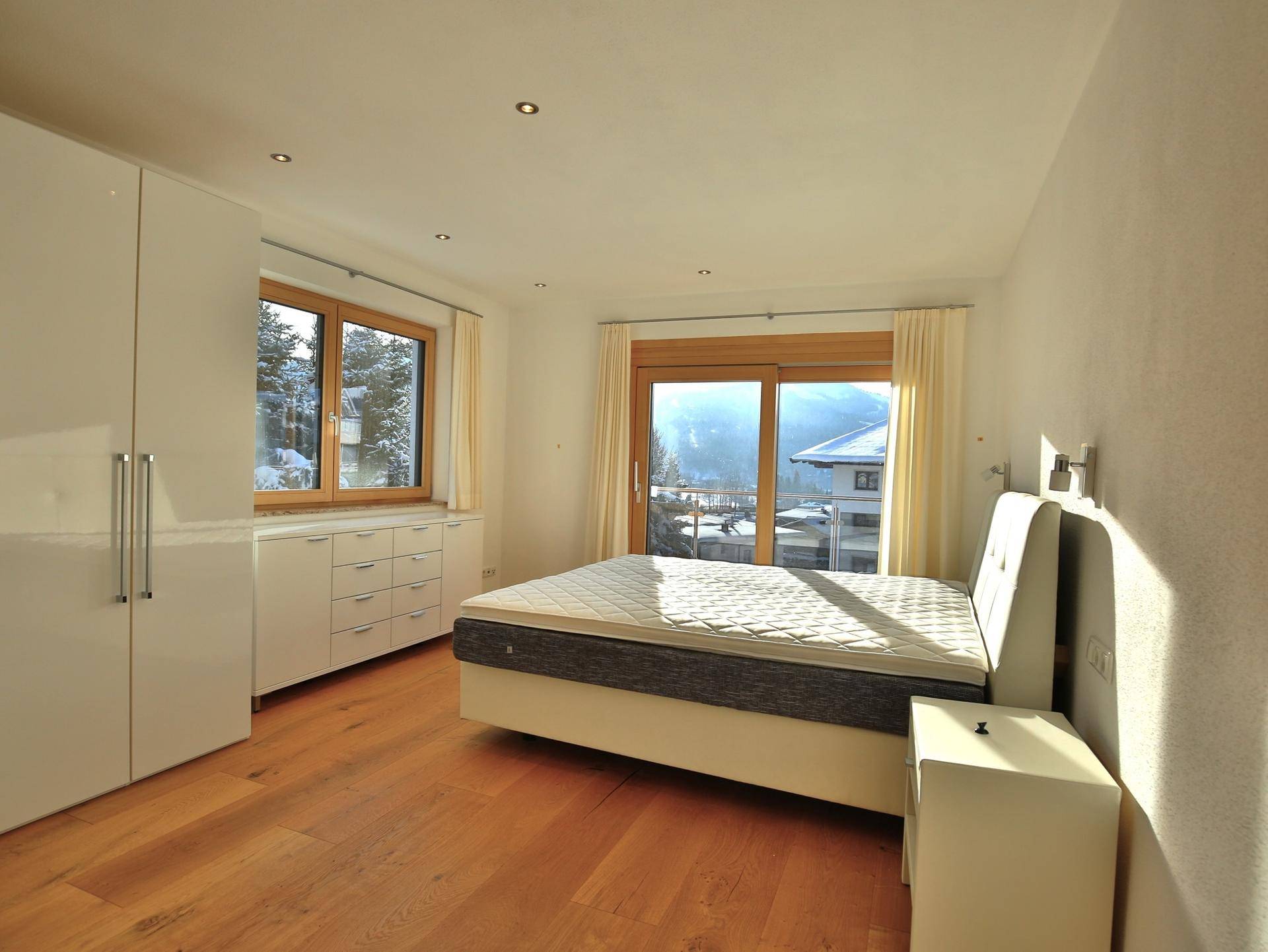Helles Schlafzimmer mit modernen weißen Schränken, Holzboden und Zugang zu einem Balkon mit Bergblick.