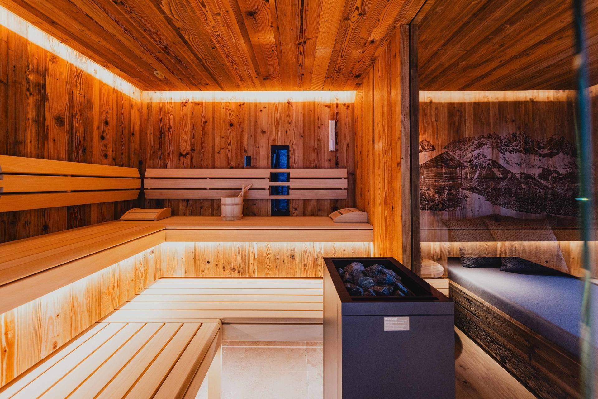 Moderne Holzsauna mit Bänken, Heizofen und stimmungsvoller indirekter Beleuchtung.