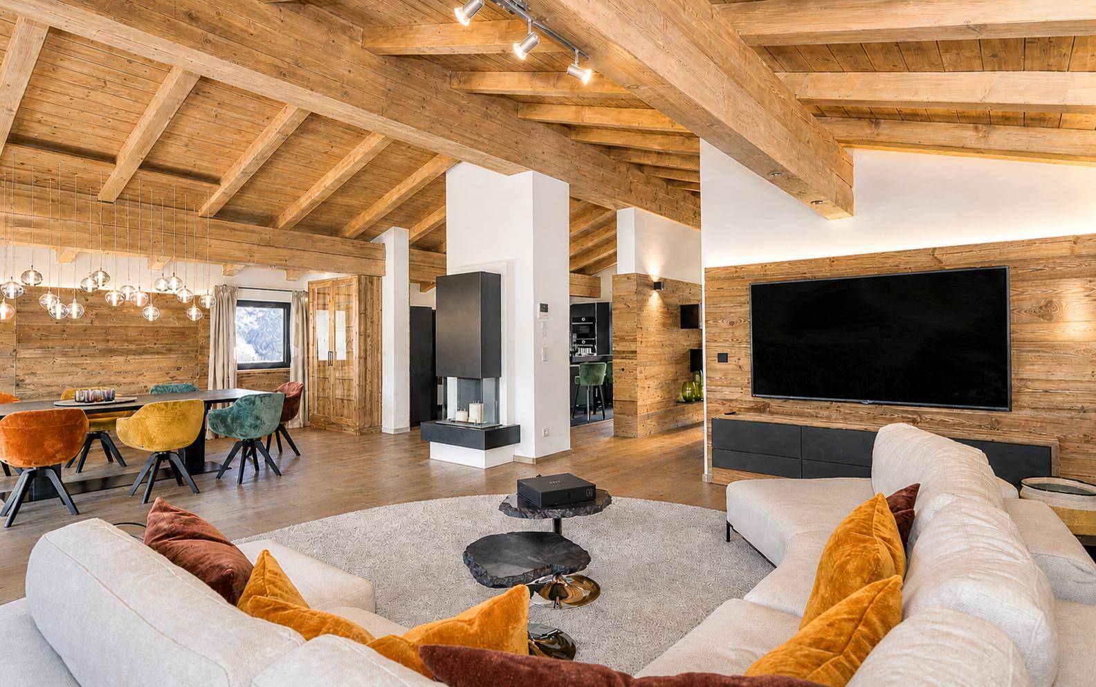 Offener Wohn- und Essbereich mit Holzbalkendecke, modernem Kamin und großem Fernseher.