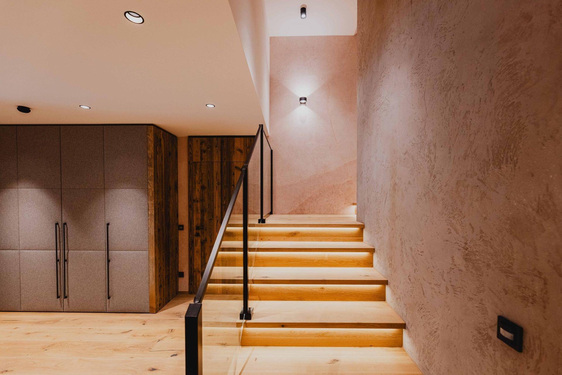 Elegante Holztreppe mit indirekter Beleuchtung und modernem Geländer im Flur.