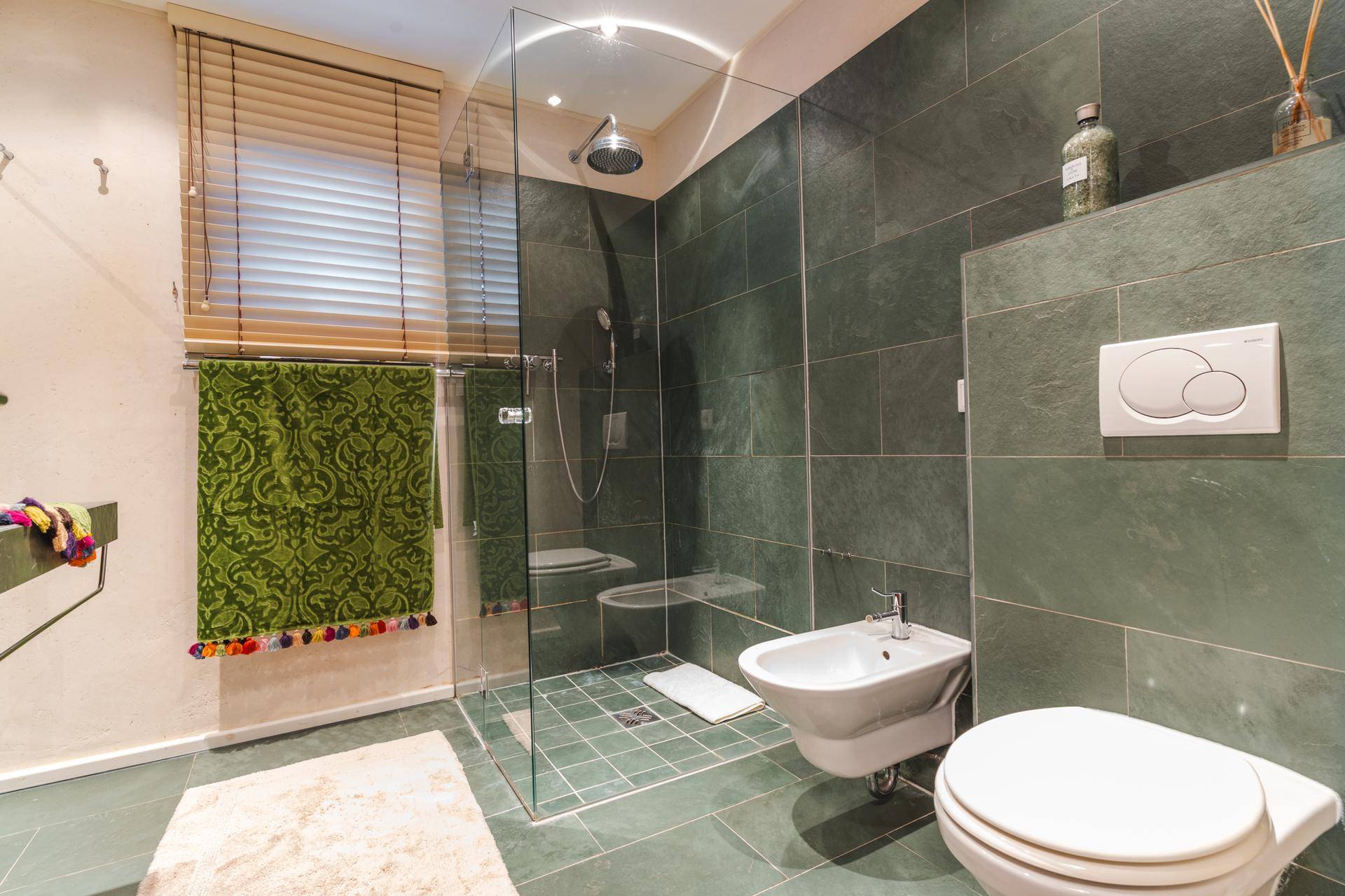 Modernes Badezimmer mit großer begehbarer Dusche, Bidet und dunkelgrünen Fliesen.