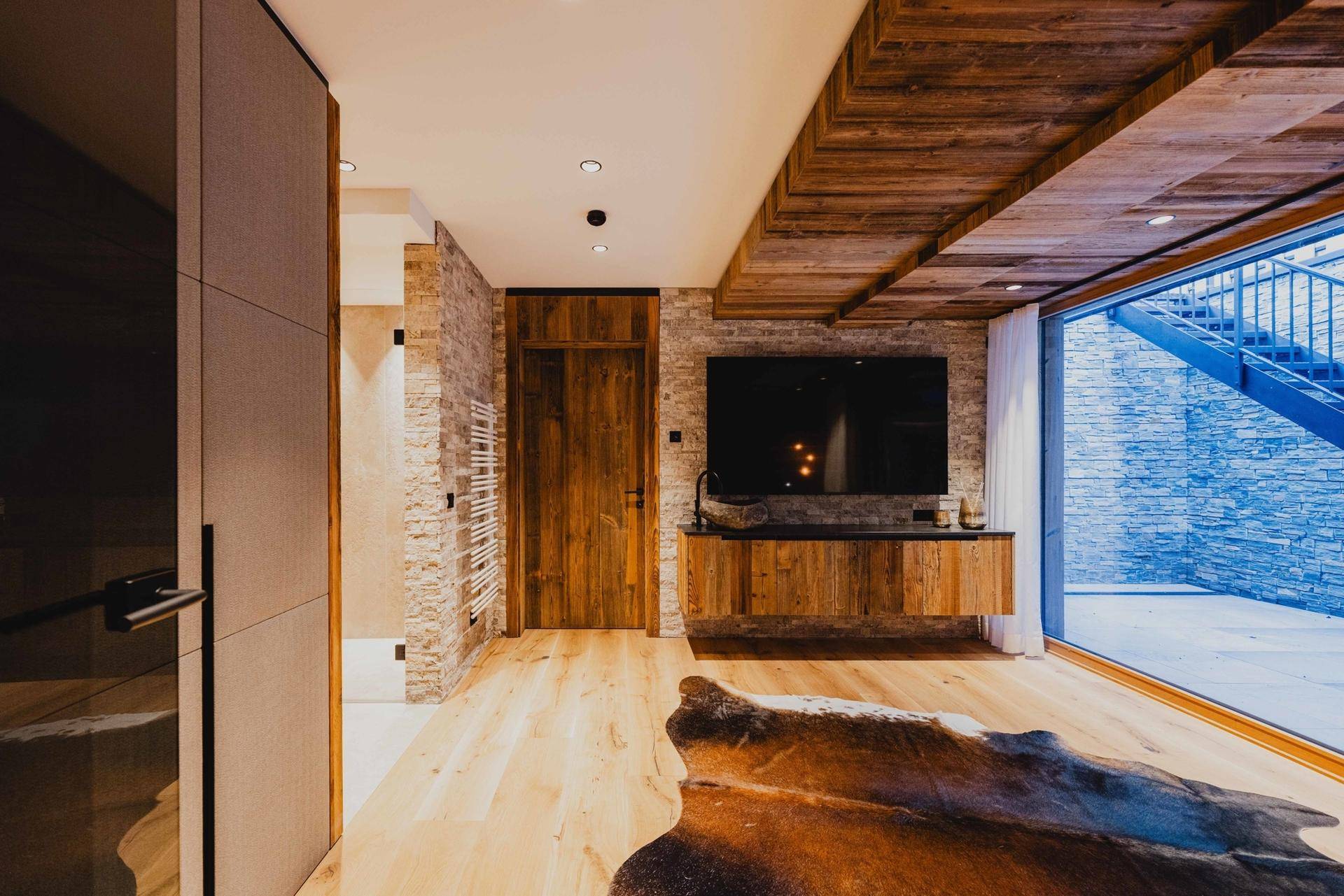 Schlafzimmer oder Lounge-Bereich mit Holzboden, Steinwand und Zugang zu einem Außenbereich.