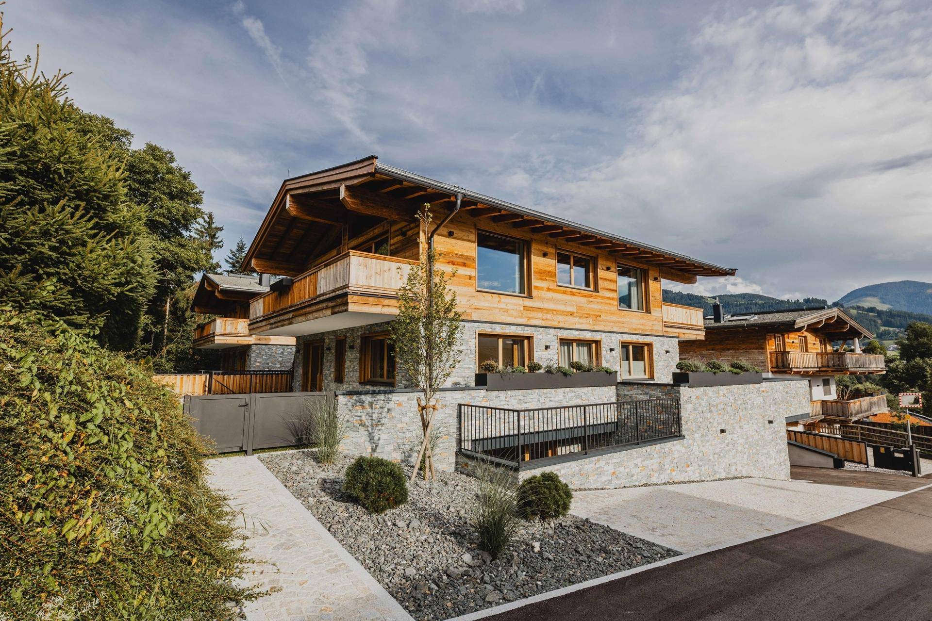 Exklusives Chalet mit moderner Holz- und Steinfassade, umgeben von gepflegter Landschaftsgestaltung und Zufahrt.