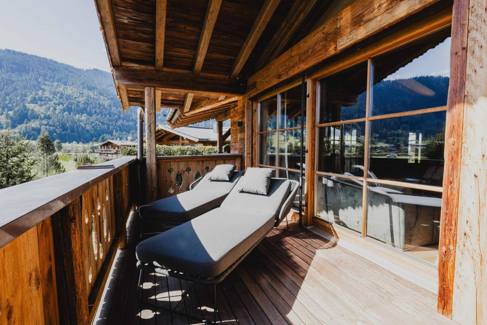Sonniger Holzbalkon mit Liegestühlen und Panoramablick auf die umliegende Berglandschaft.