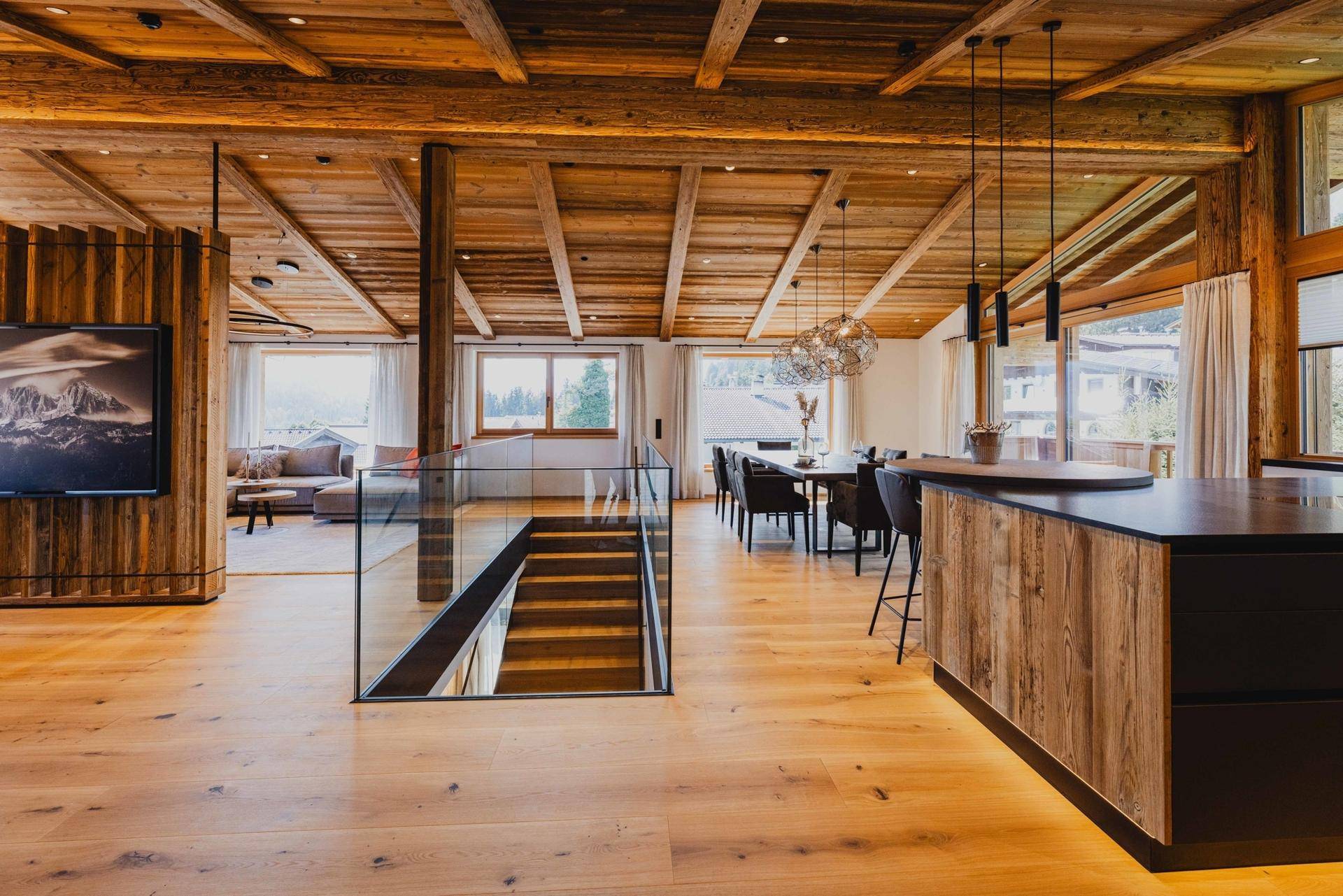 Geräumiger offener Wohnbereich mit Holzbalkendecke, Parkettboden und moderner Treppe.