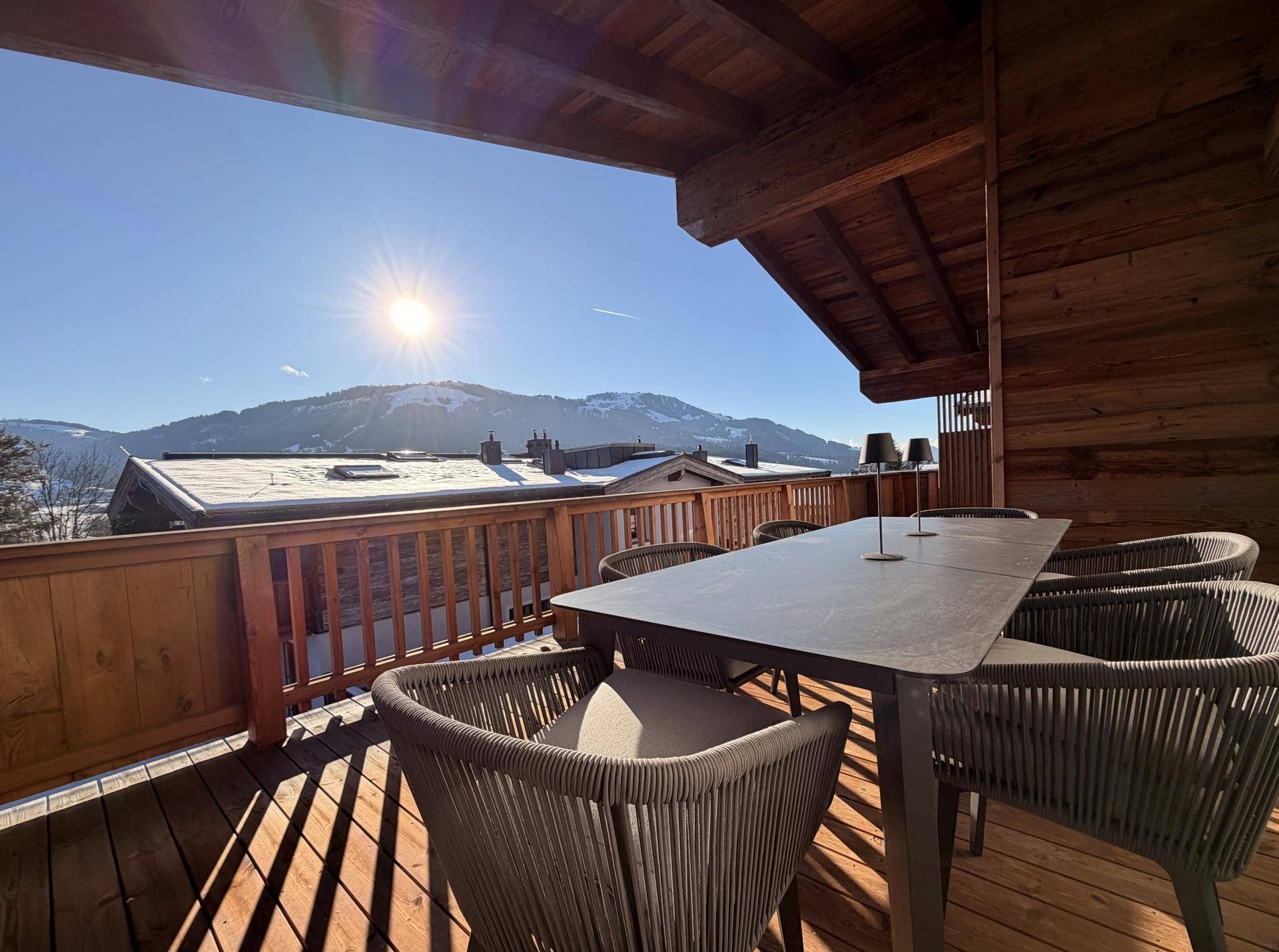 Sonnige Holzterrasse mit Esstisch und Stühlen, bietet einen weiten Blick auf die verschneite Berglandschaft.