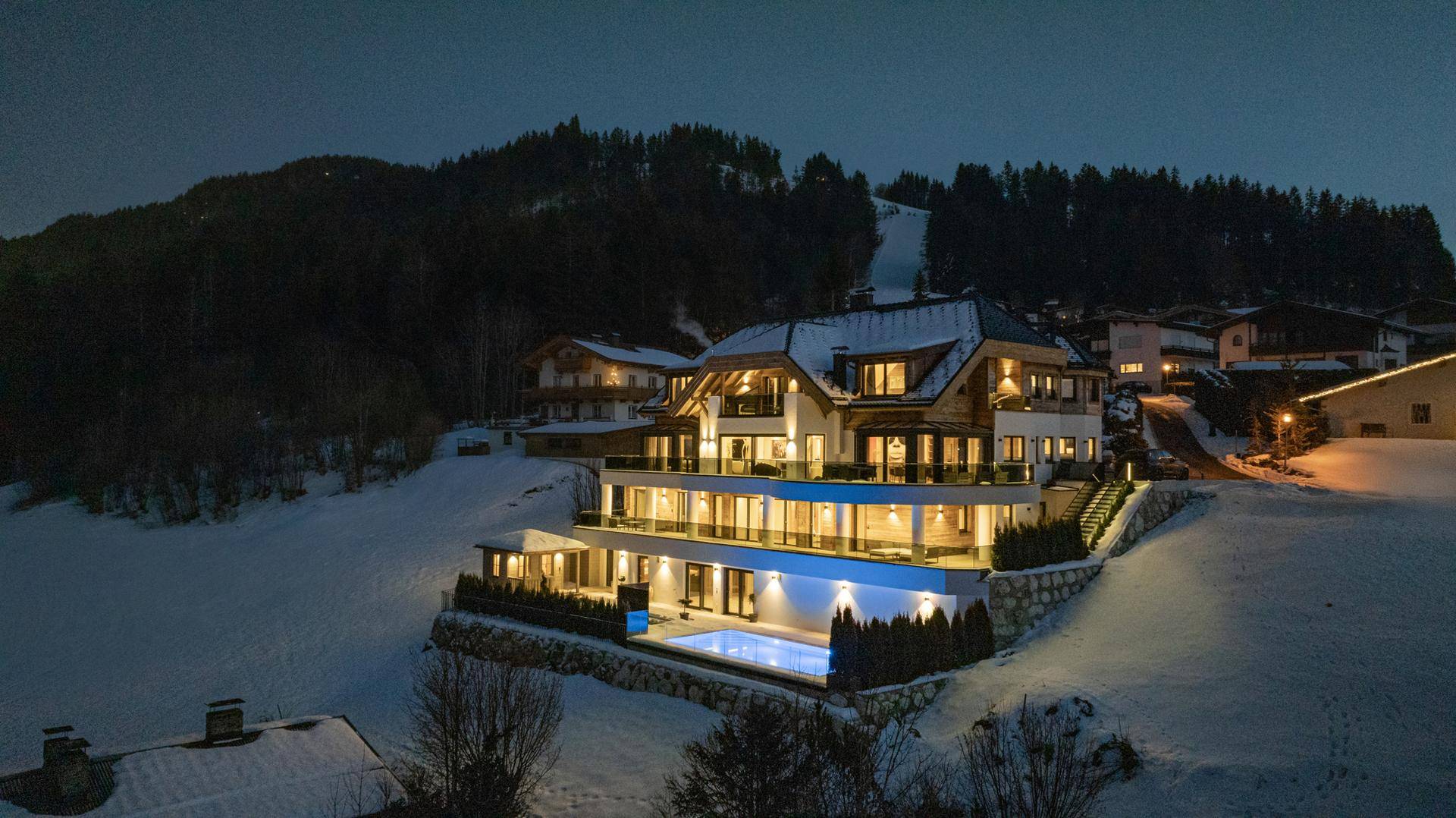 Beeindruckendes Anwesen bei Nacht mit beleuchtetem Außenpool und Bergblick.