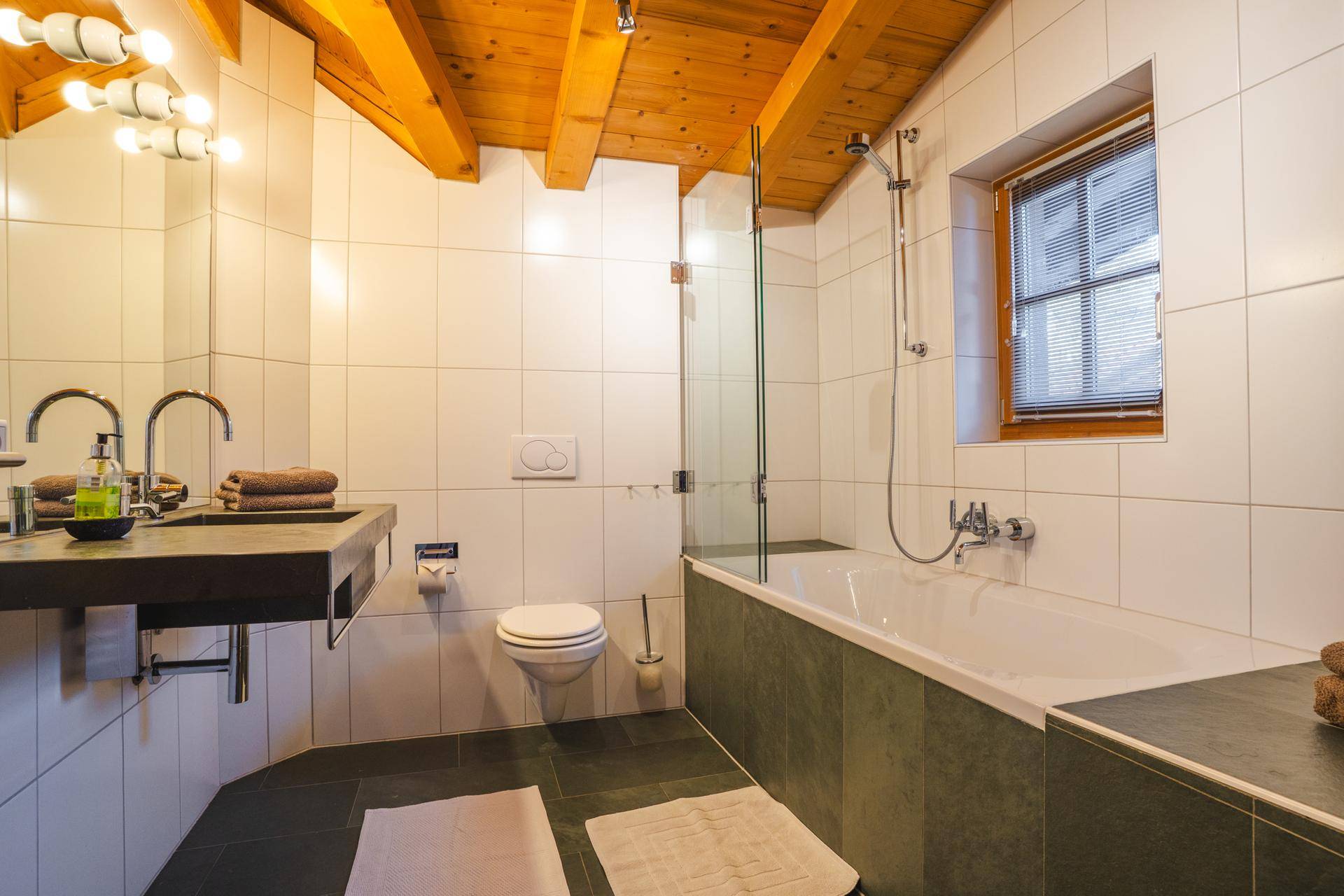 Helles Badezimmer mit Badewanne, Dusche, Doppelwaschbecken und Holzbalkendecke.