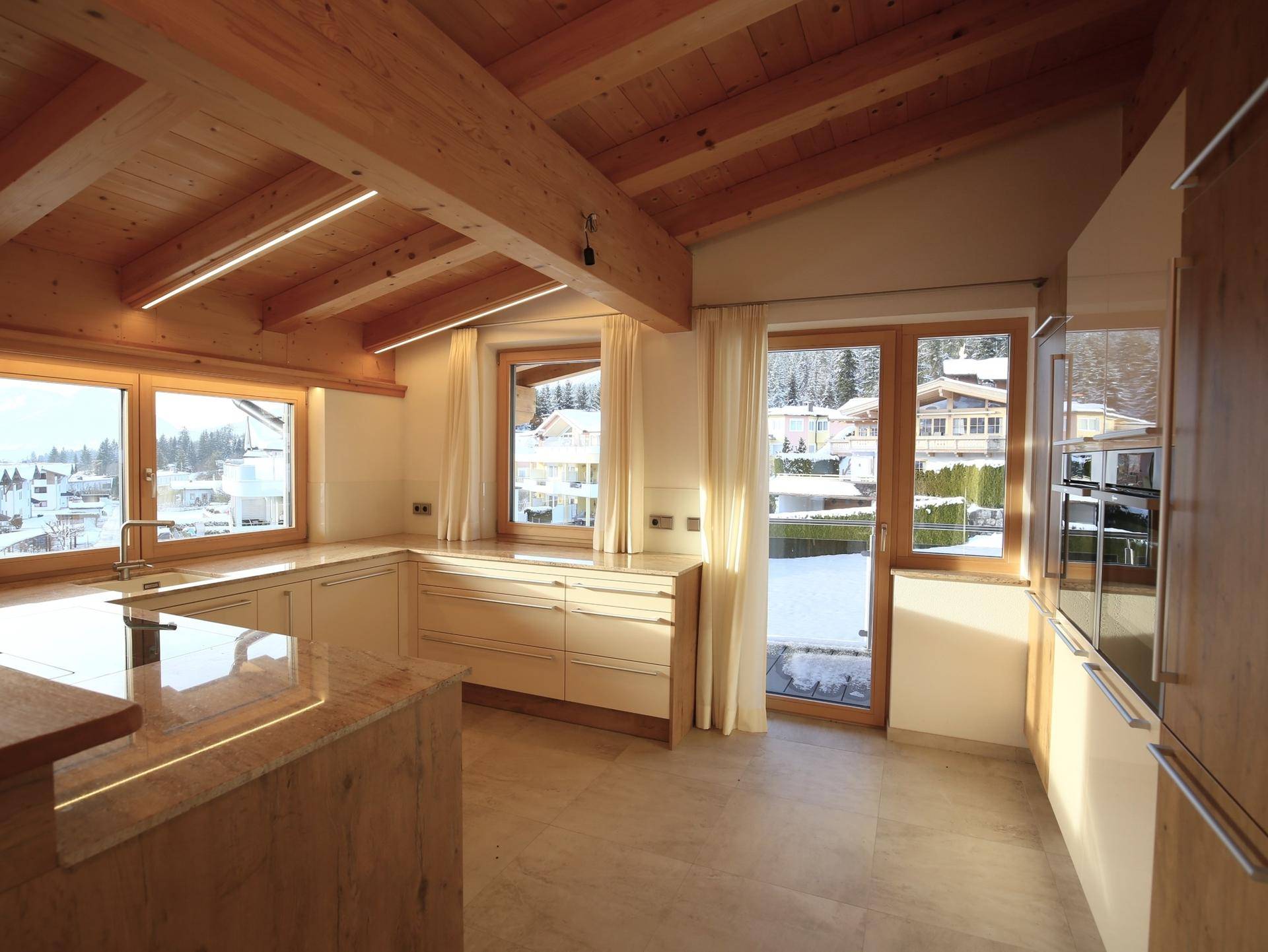 Moderne Küche mit Holzbalkendecke, Granitarbeitsplatten und Blick auf die verschneite Landschaft.
