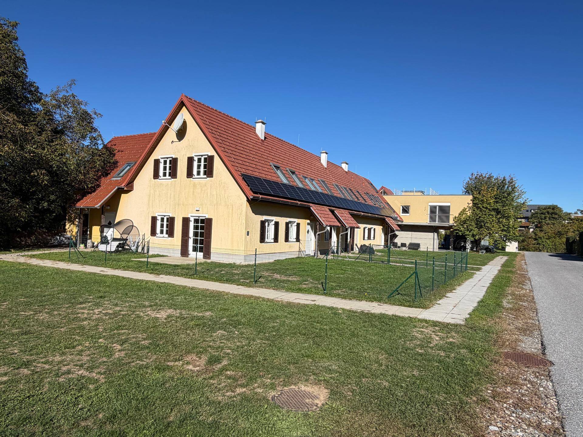 Weitwinkelansicht des gelben Hauses mit Solaranlage, rotem Dach und angrenzender Straße im Grünen.