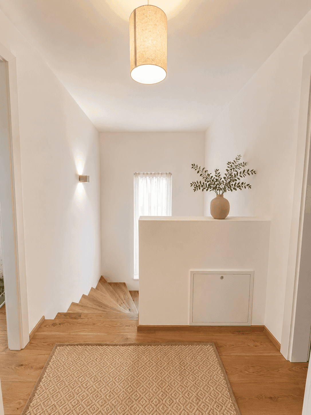 Eingangsbereich mit Holztreppe, heller Wandgestaltung und dekorativer Vase.