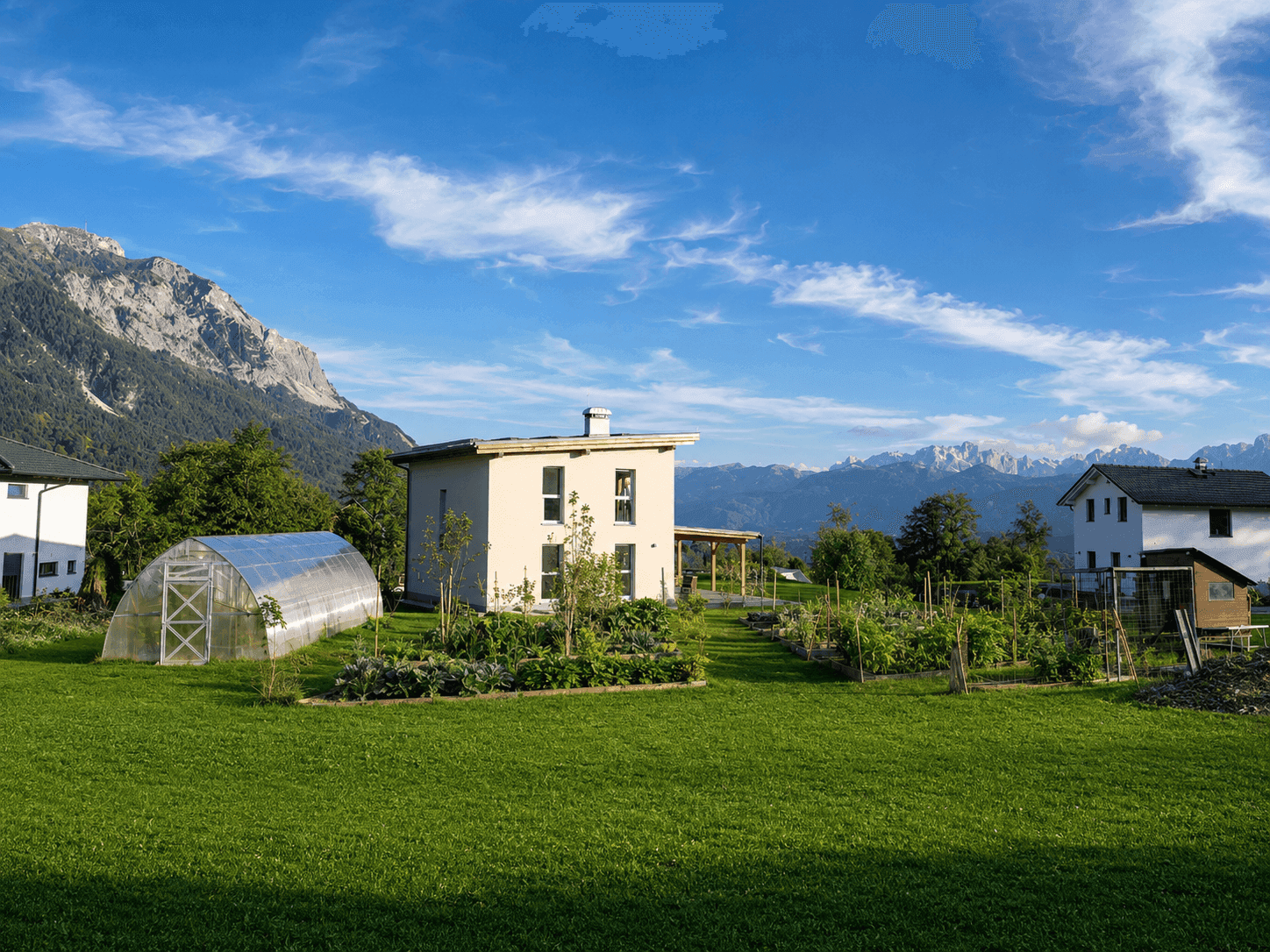 Weitläufiger Gartenbereich mit Gewächshaus und Gemüsegarten, umgeben von Bergen und ländlicher Idylle.