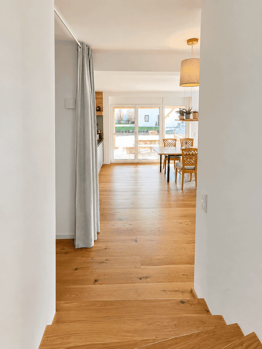 Heller Flur mit Holztreppe, der zu einem offenen Wohnbereich mit Küche führt.