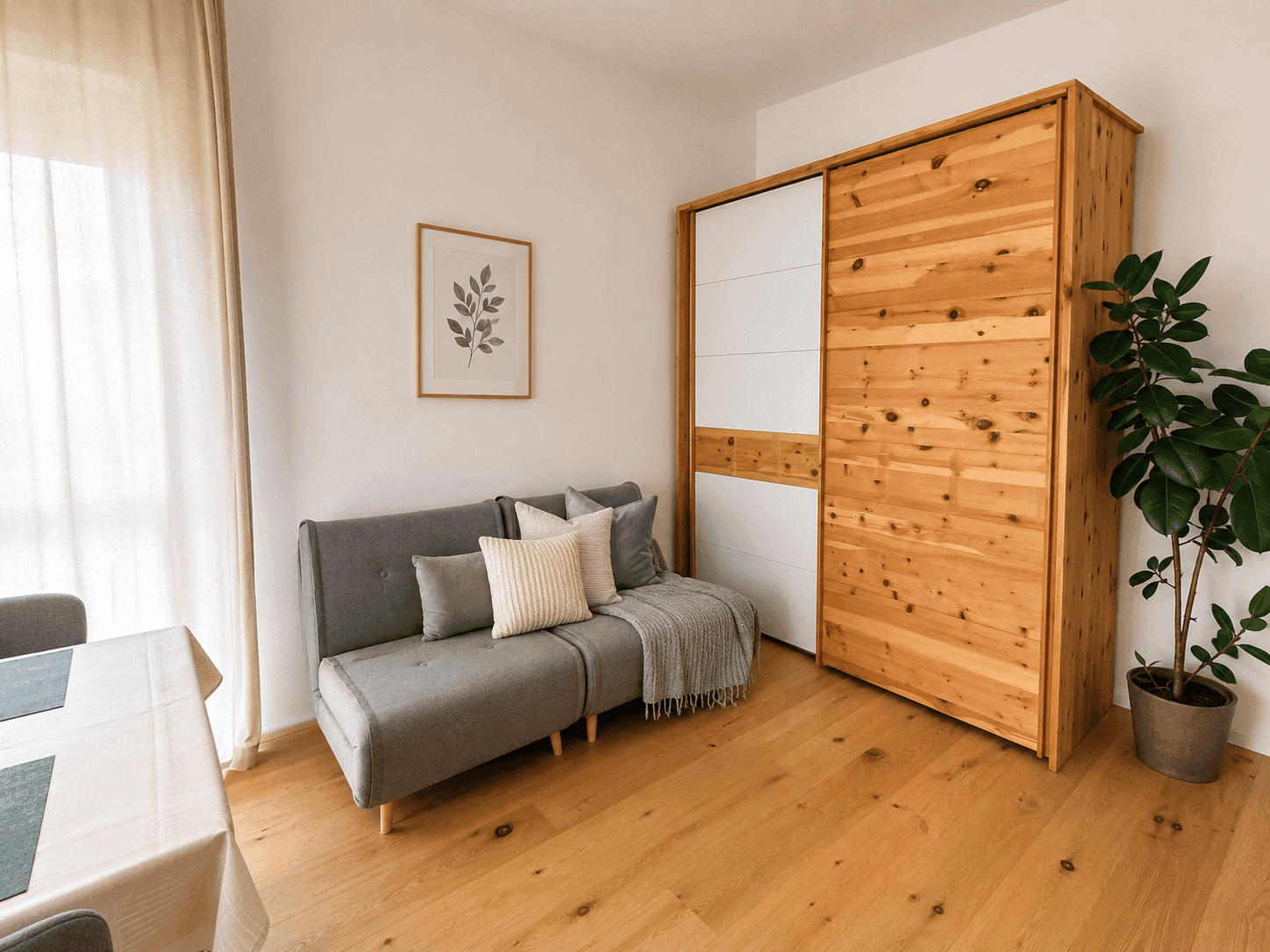 Helles Zimmer mit Schlafsofa, großem Holzschrank und Eichenparkettboden.