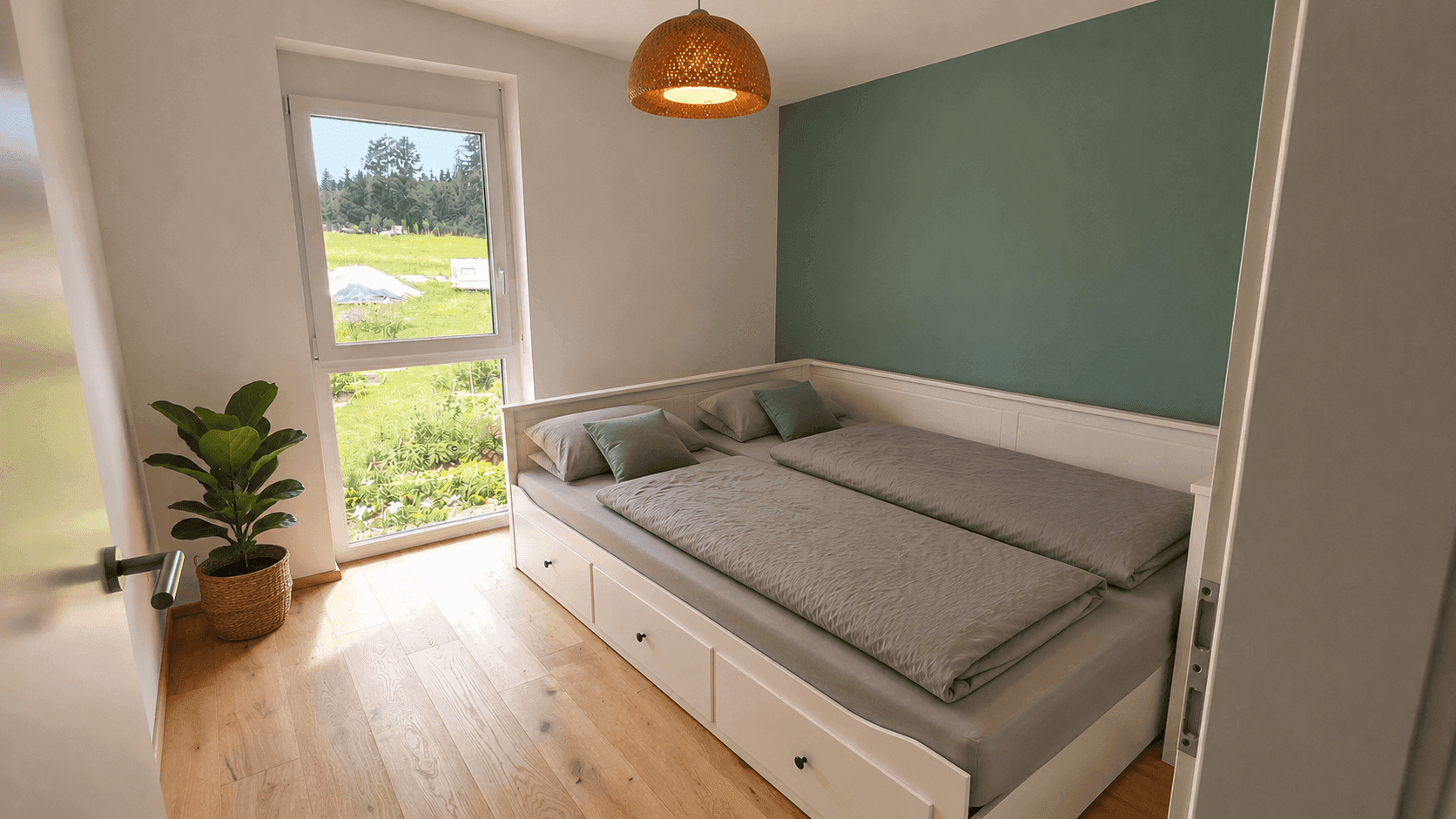 Helles Schlafzimmer mit ausziehbarem Bett, Holzboden und Blick ins Grüne.
