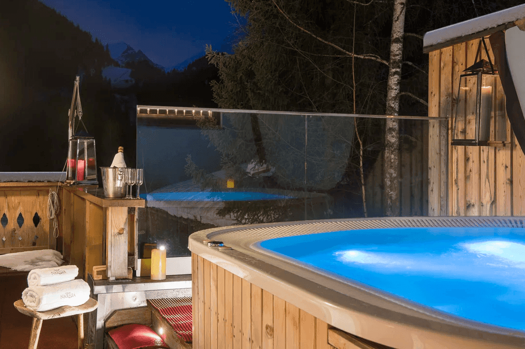 Beleuchteter Whirlpool im Freien bei Nacht, umgeben von Holzverkleidung und winterlicher Atmosphäre.