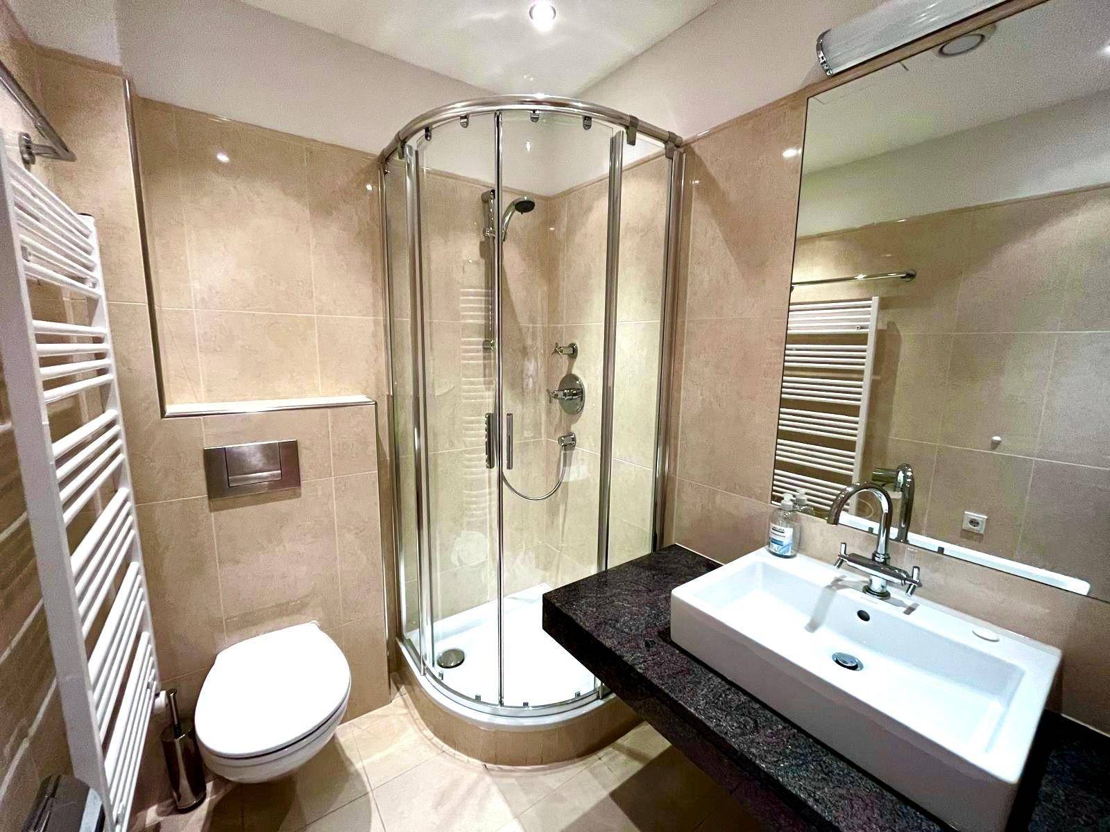Helles Badezimmer mit Duschkabine, WC, Einzelwaschbecken und beheiztem Handtuchhalter.