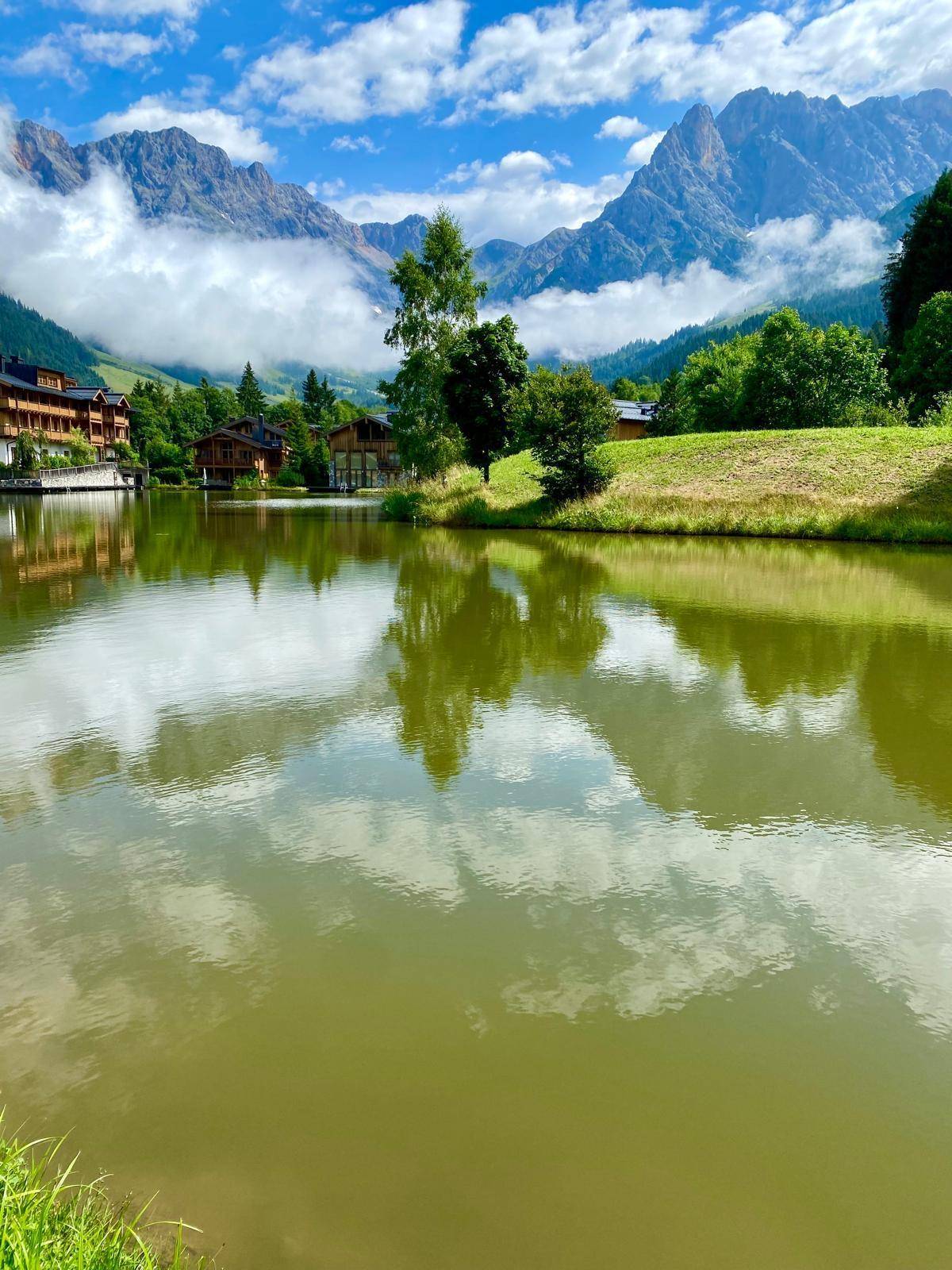 Ruhiger See mit Spiegelungen der Wolken und umliegenden Bergen in einer idyllischen Landschaft.