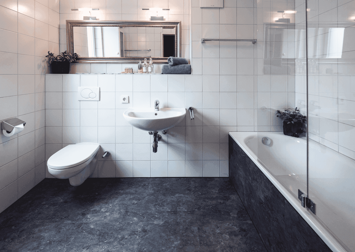 Helles Badezimmer mit weißen Fliesen, Waschbecken, Toilette und Badewanne mit Duschwand.